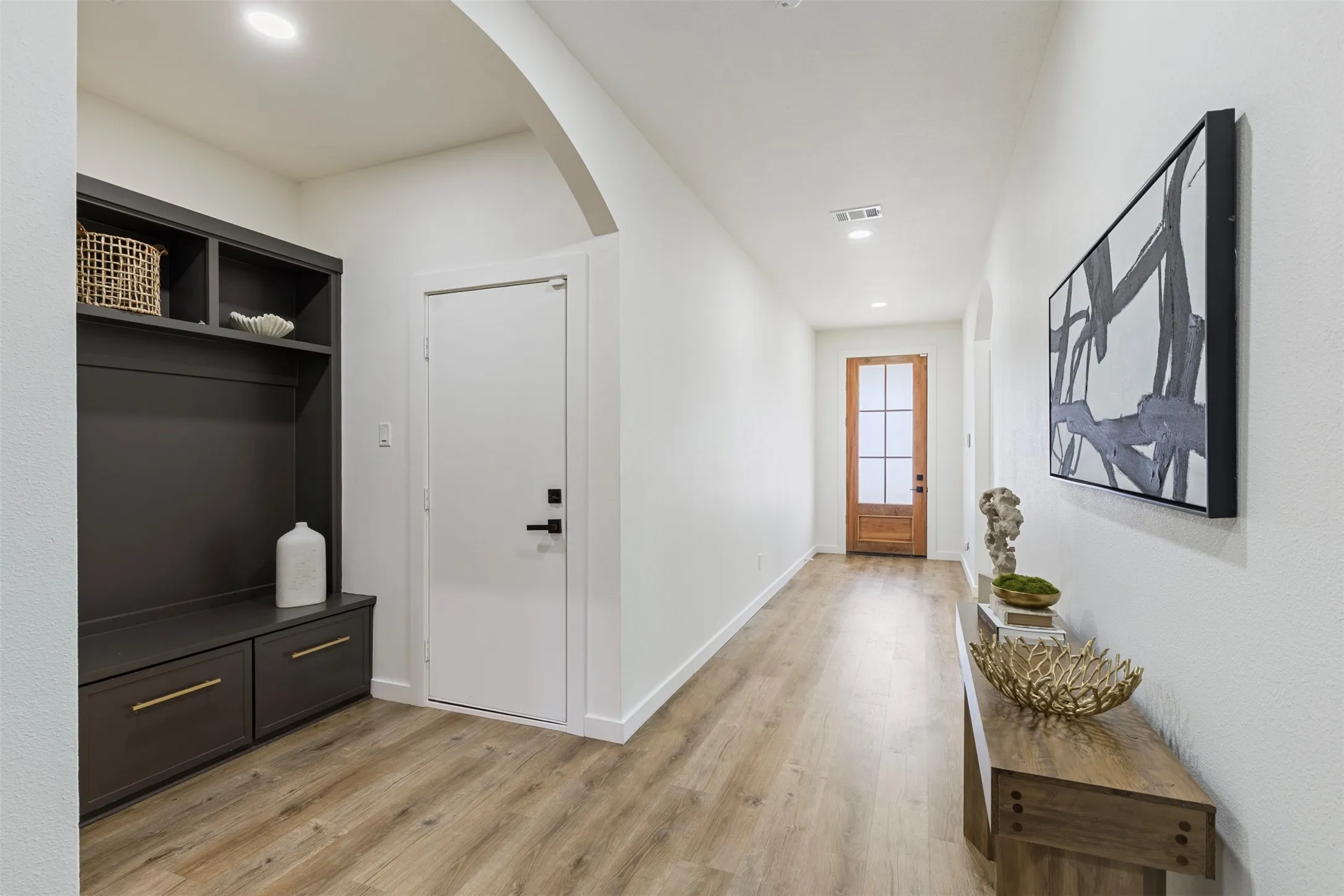 Wood-finish flooring throughout, built-in storage bench with shelving and drawers, recessed lighting, and an arched entryway
