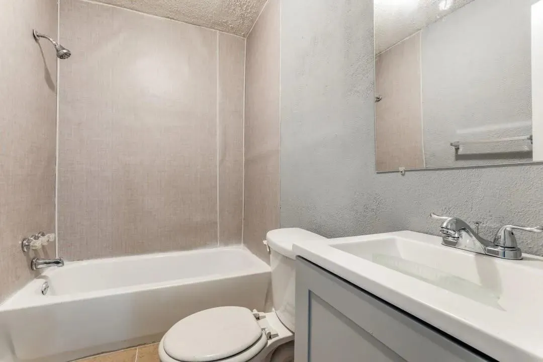 Bathroom featuring a shower-tub combination, a vanity with an integrated sink, a wall-mounted mirror, and a commode