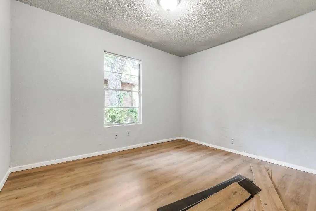 Light grey walls, wood-finish flooring, and a single window with white trim