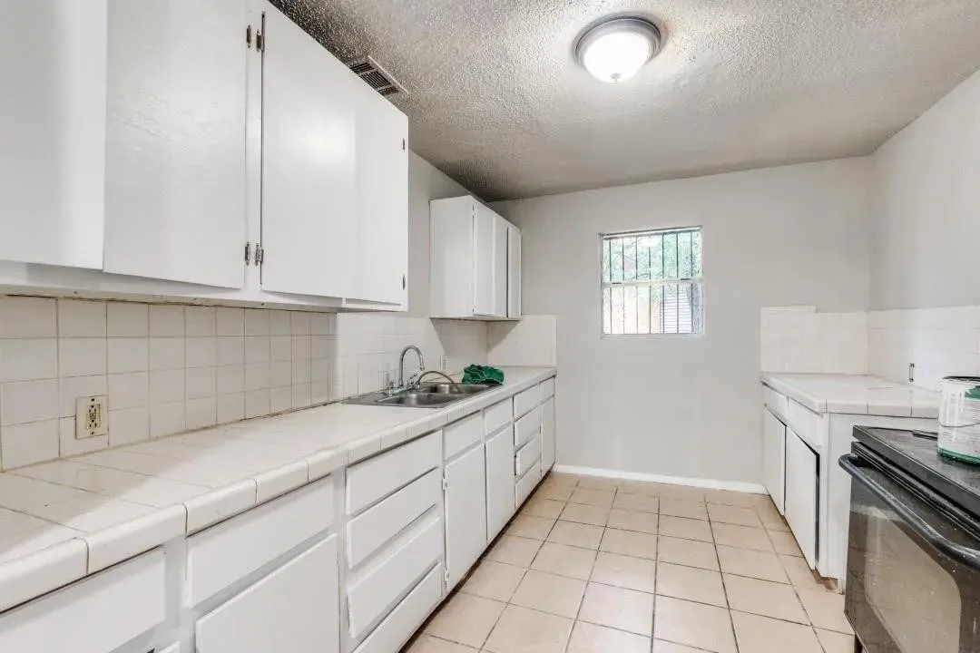 Kitchen featuring white cabinetry, tile countertops, tile backsplash, stainless steel sink, and tile flooring