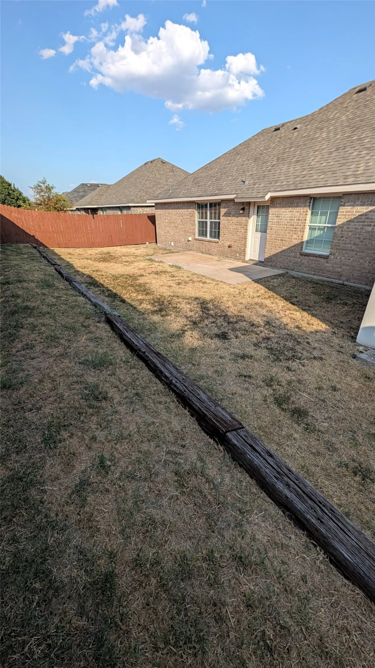 Long back yard with patio and storage shed at back.