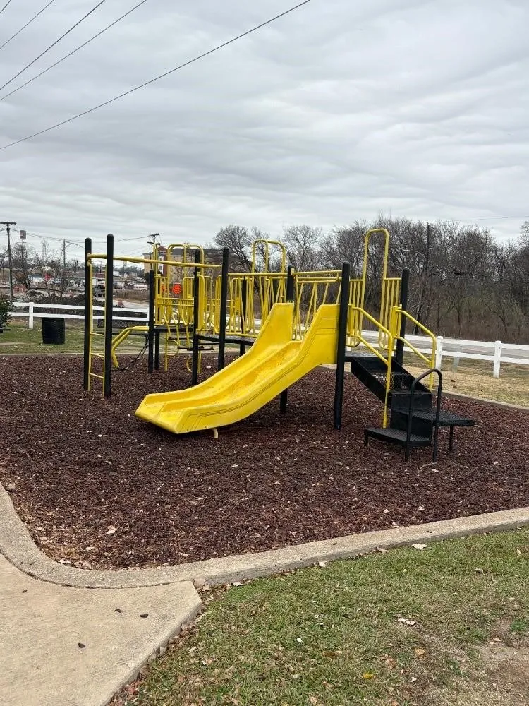 Playground structure with yellow slides and black stairs, surrounded by wood mulch