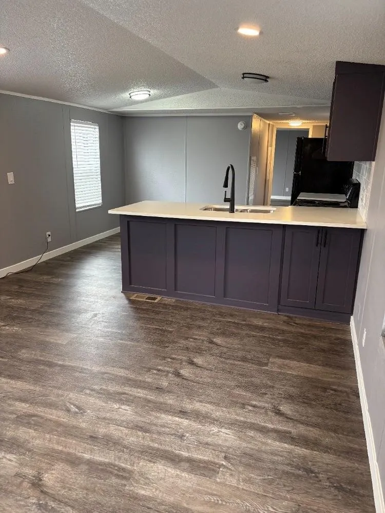 Kitchen island with integrated sink, white countertops, black gooseneck faucet, black appliances, and wood-finish flooring
