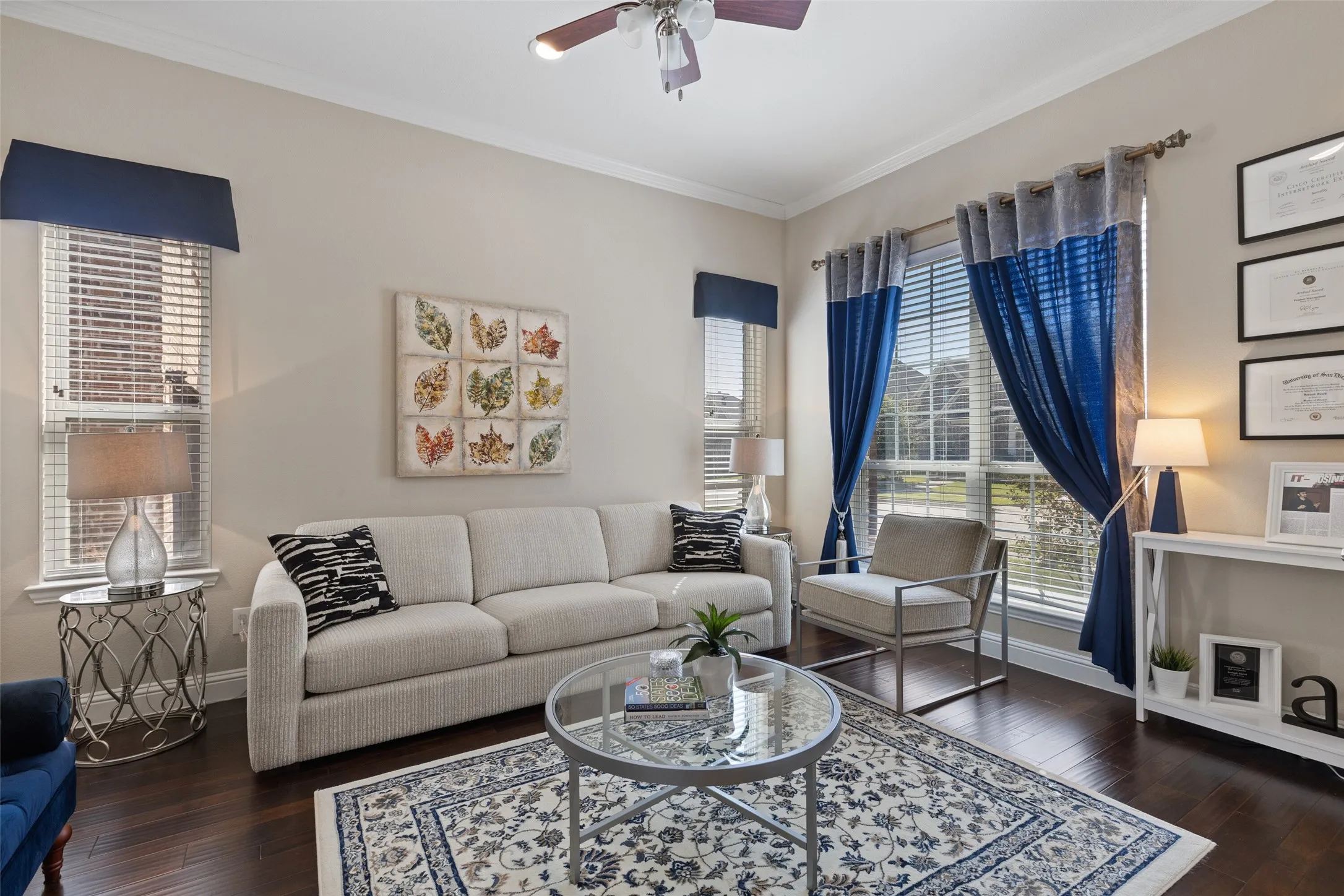 Wood-finish flooring, crown molding, a ceiling fan with integrated lighting, and multiple windows with blinds