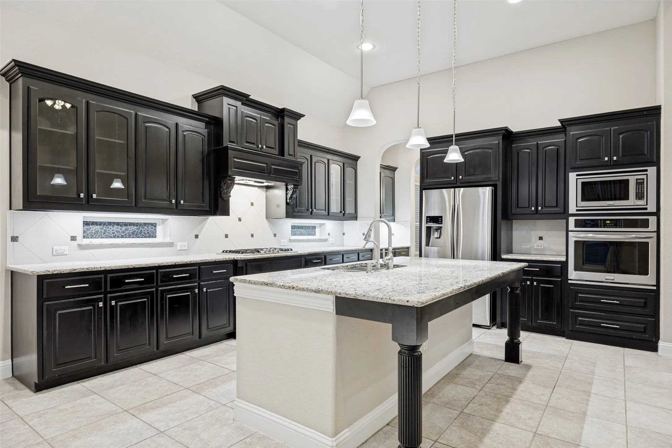 Kitchen featuring dark wood cabinetry, light-toned countertops, stainless steel appliances, a center island with a sink, and tile flooring