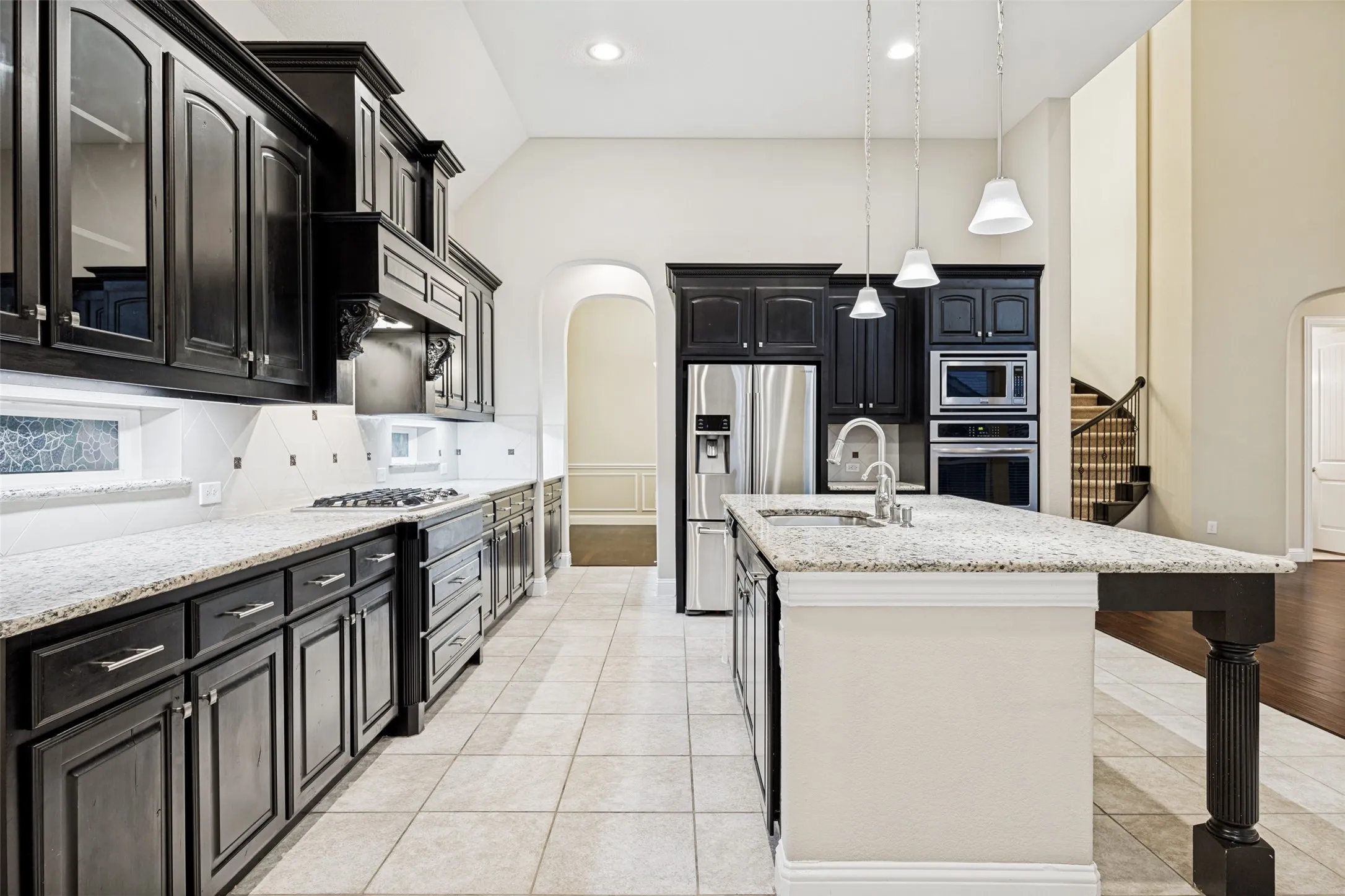 Kitchen featuring dark cabinetry, light countertops, stainless steel appliances, a center island with sink, and tile flooring