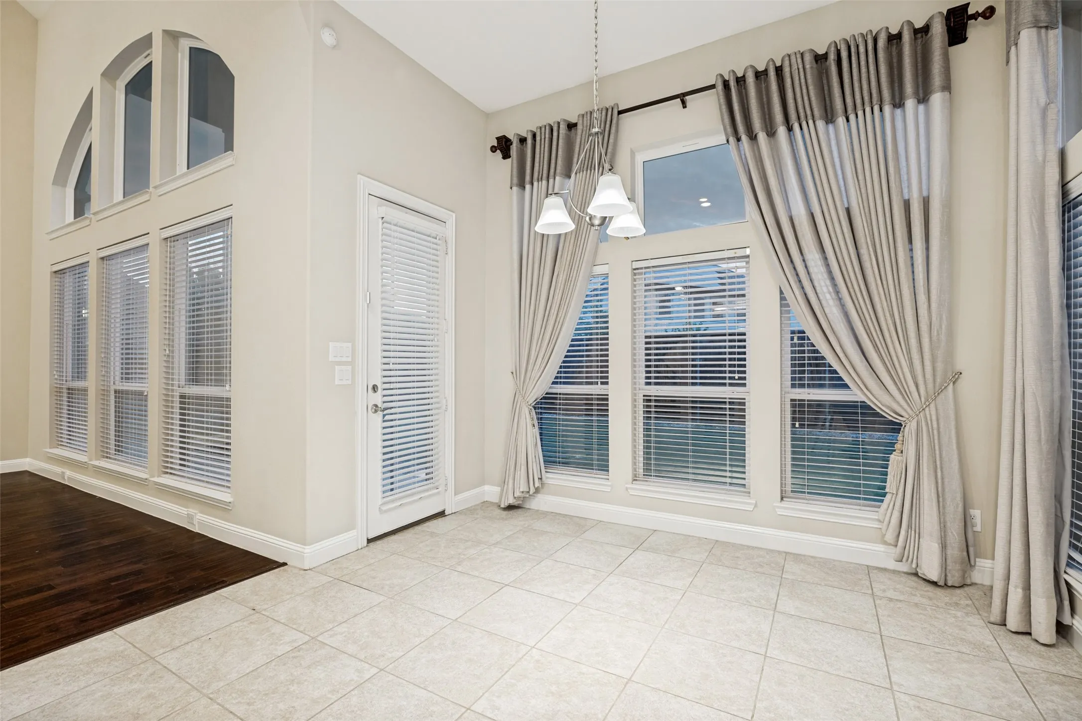 High ceilings with an arched window, white door with integrated blinds, and a tiled floor