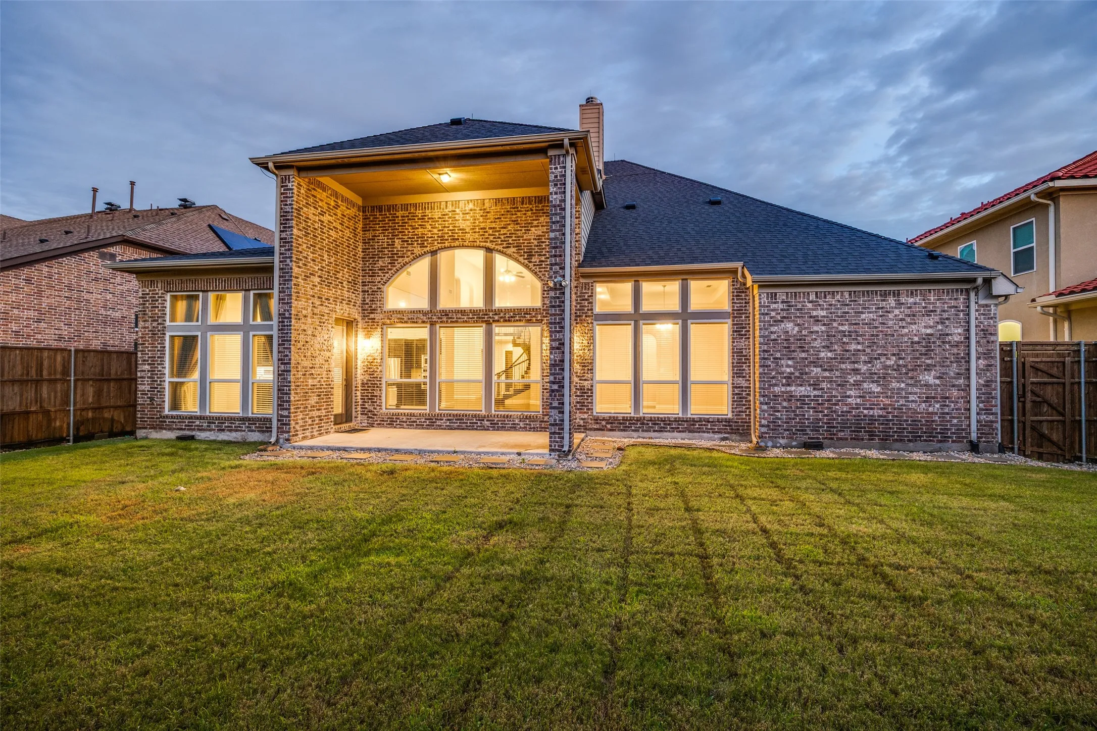 Full brick exterior with a covered patio, expansive lawn, and architectural windows including an arched feature window