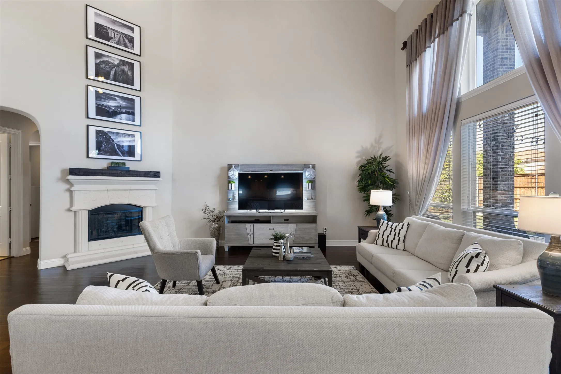 Vaulted ceiling with high windows, dark wood-finish flooring, white stone-clad fireplace, and an arched doorway