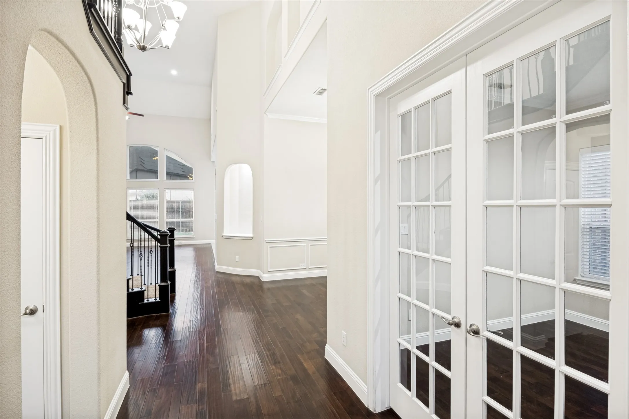 Dark wood-finish flooring, white French doors, wainscoting, arched architectural details, and a multi-level ceiling