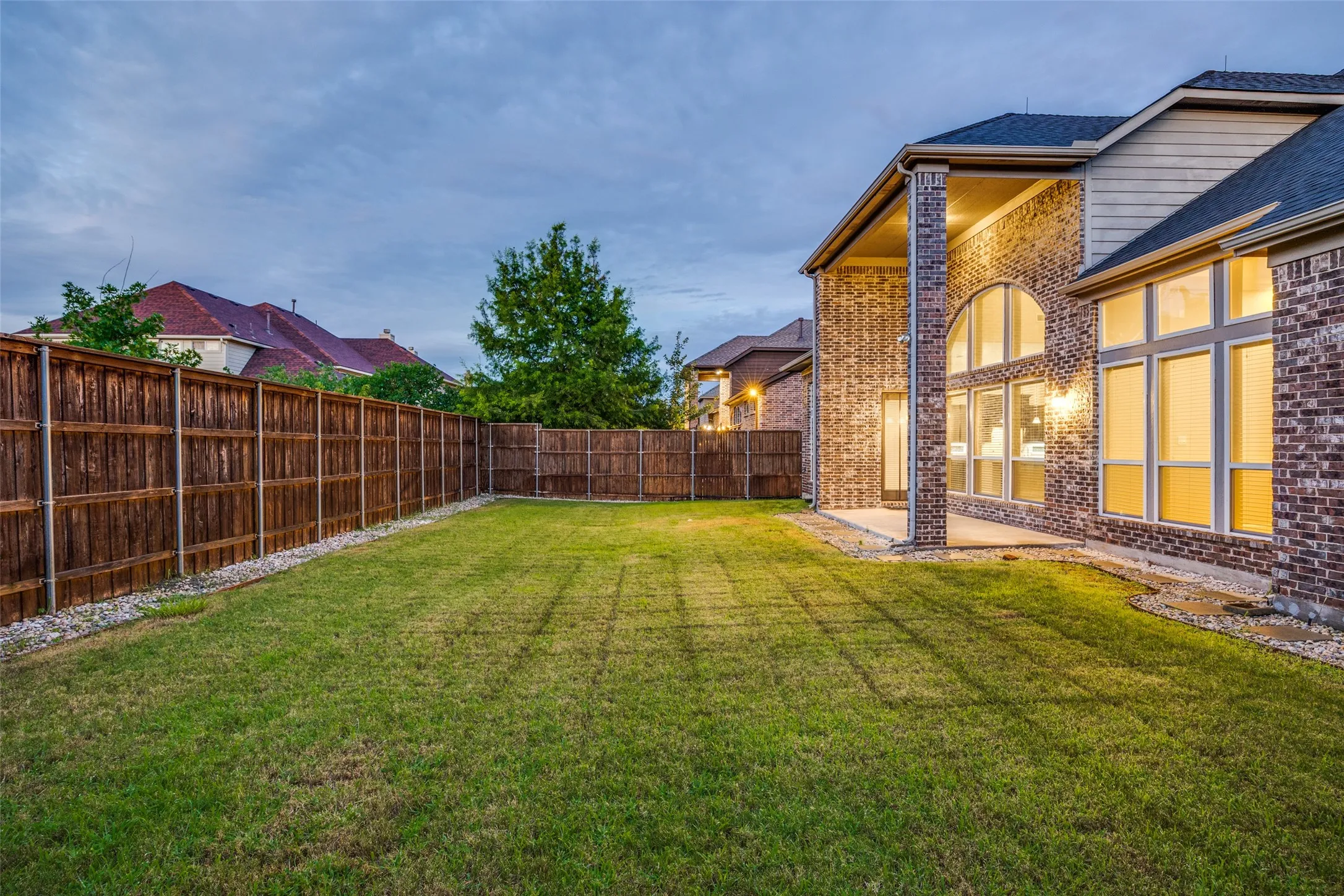 Expansive backyard featuring a manicured lawn, full privacy fencing, and a covered patio with brick columns