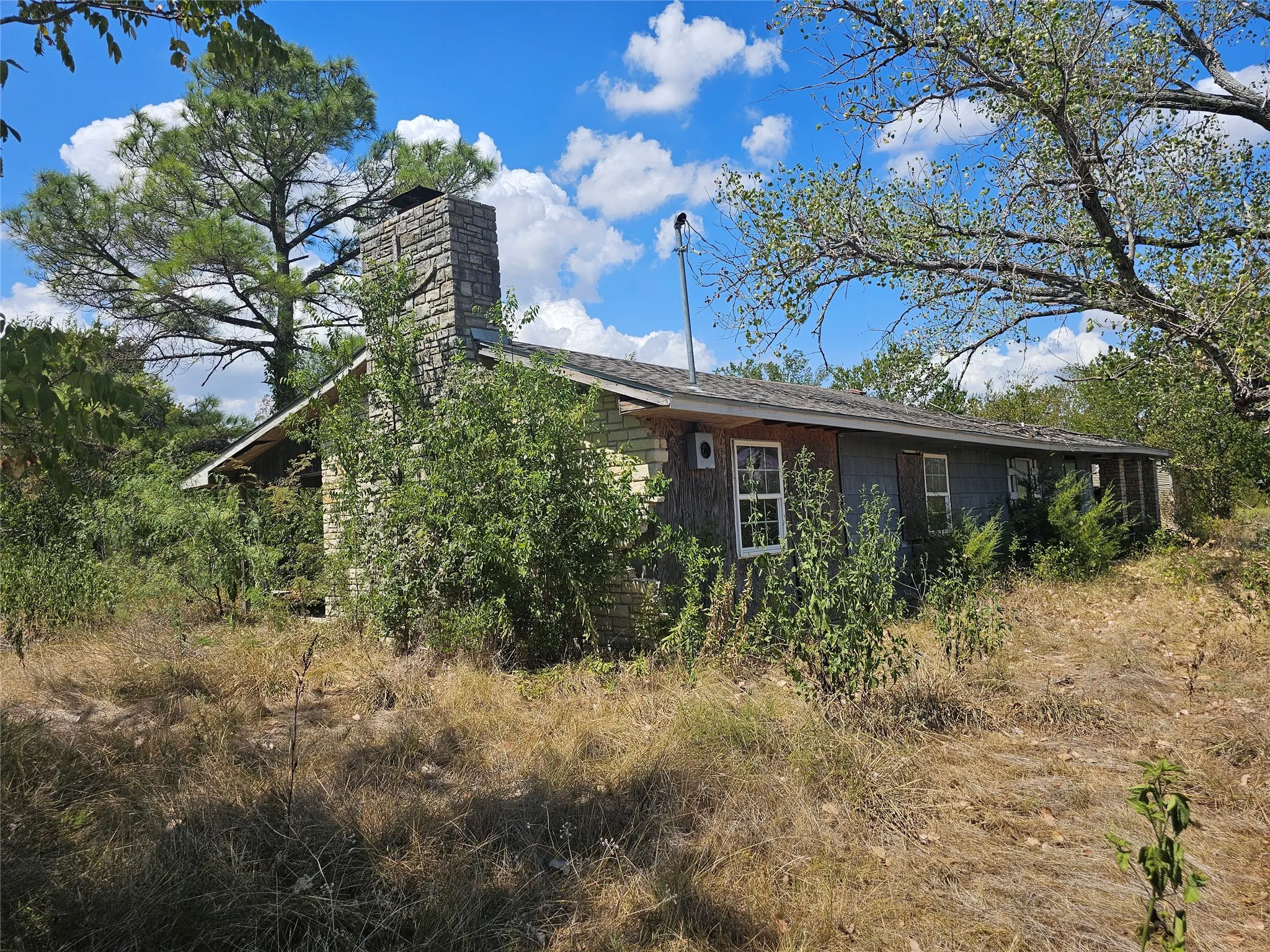Stone-clad chimney, gable roofline, multiple windows, and natural landscaping surround the structure