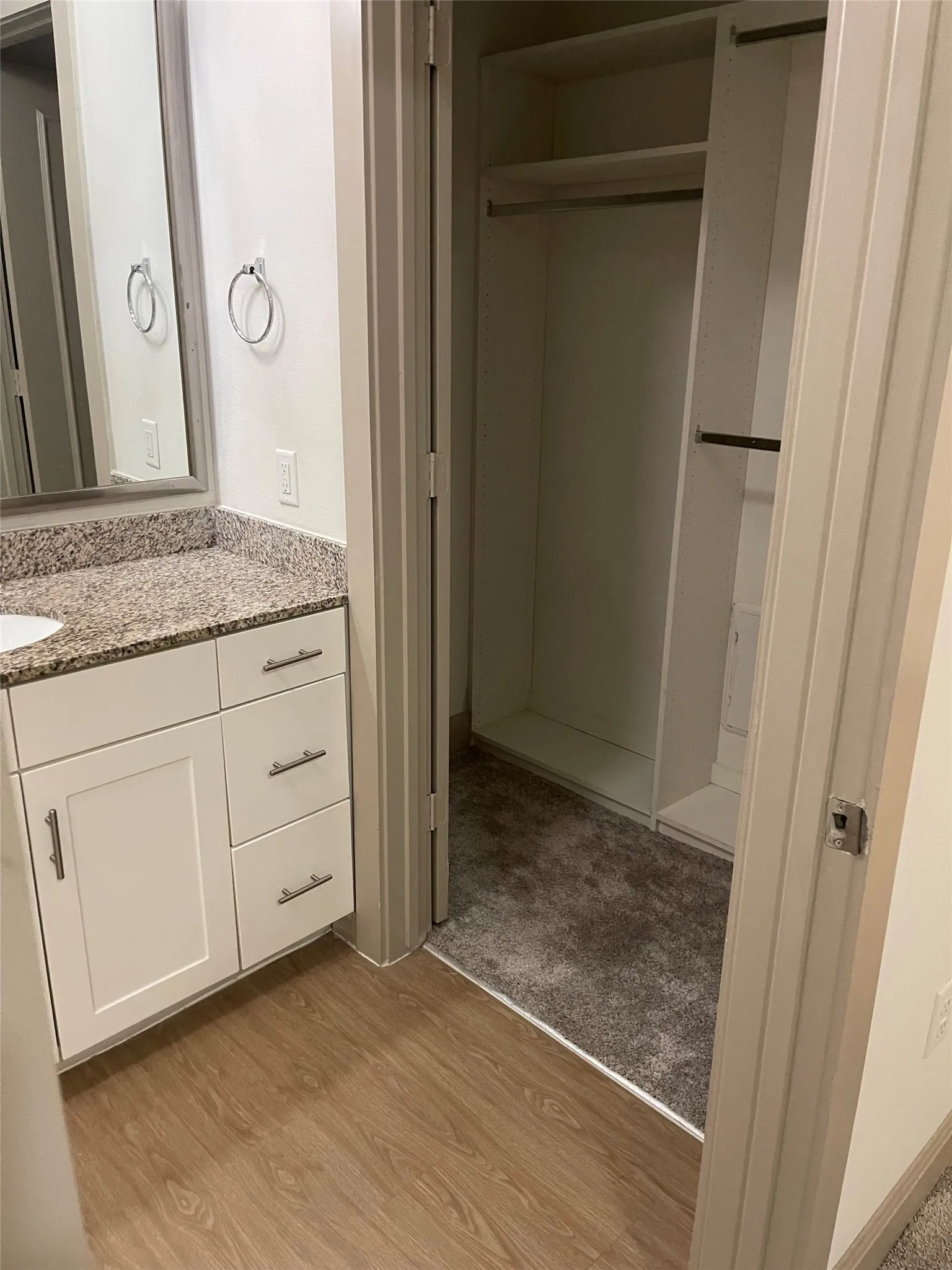 White shaker-style cabinetry with brushed nickel hardware, speckled countertop, wood-finish flooring, and a walk-in closet with built-in shelving