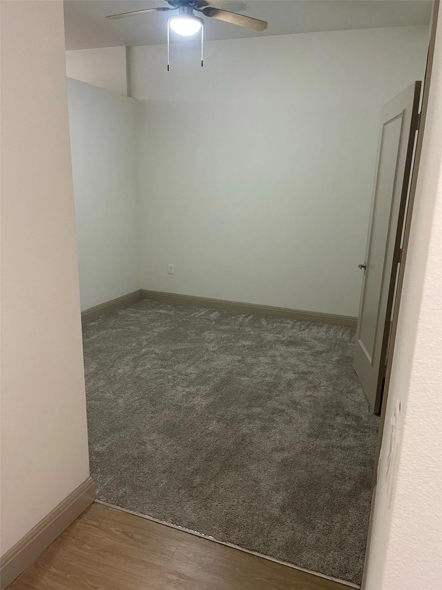 Textured carpet flooring, neutral wall tones, ceiling fan with integrated lighting, and a paneled interior door