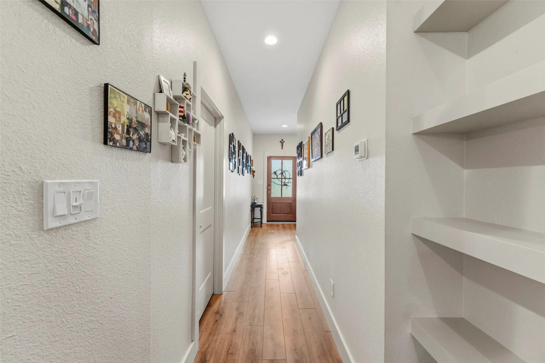 Hallway featuring wood-finish flooring, recessed lighting, built-in shelving, and a paneled entry door with frosted glass detailing