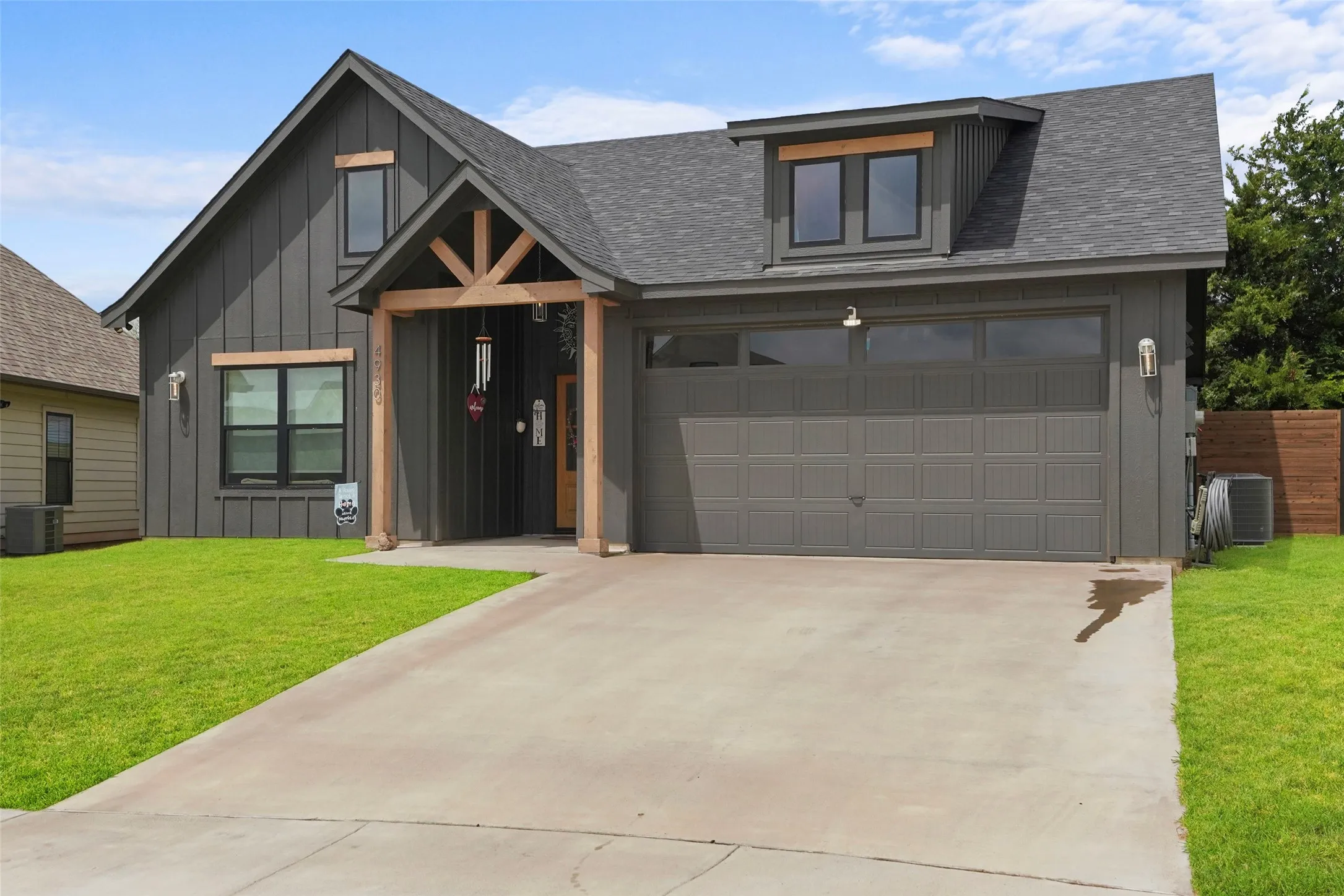 Board and batten exterior with wood beam accents, attached garage, dormer window, and concrete driveway