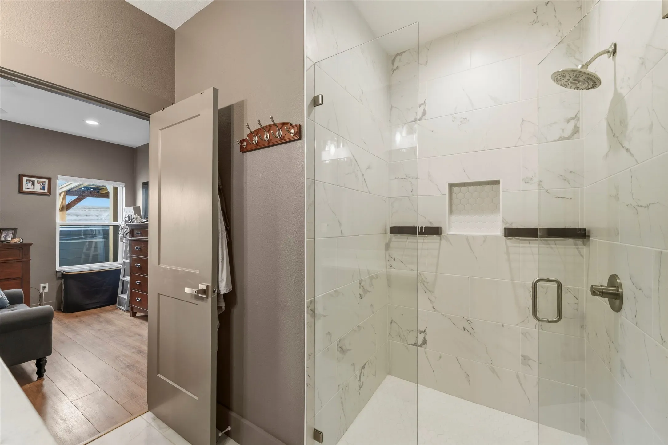 Spacious shower enclosure featuring large-format white tile with gray veining, a built-in niche, and a brushed nickel rain shower head