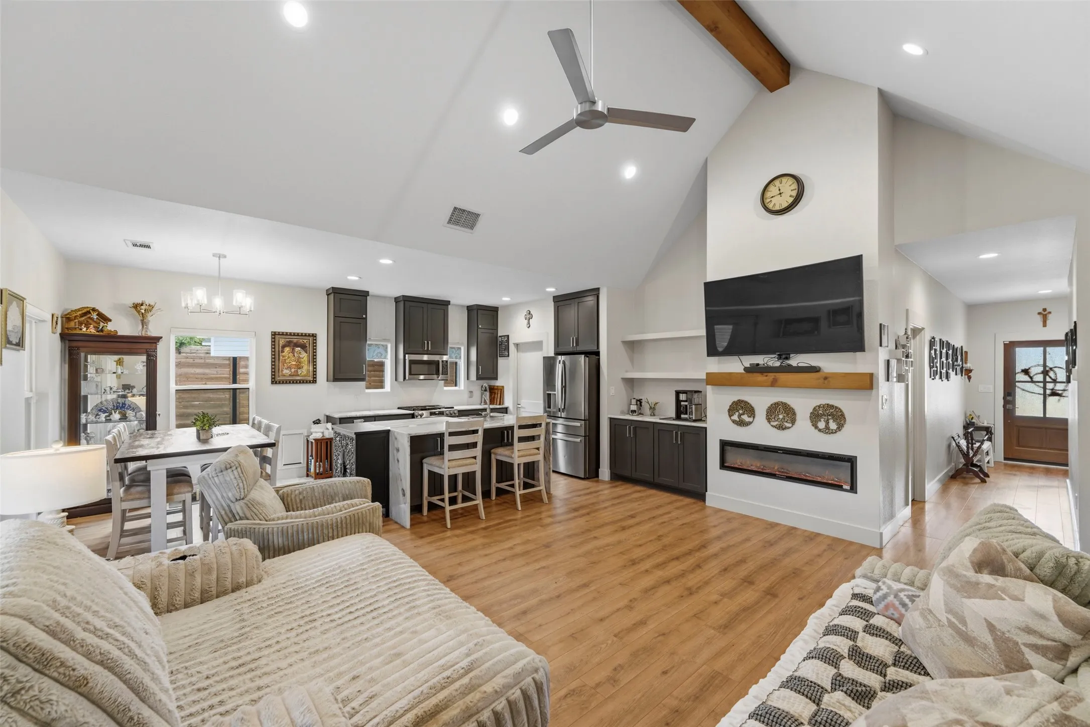 Open-concept living space featuring wood-finish flooring, a vaulted ceiling with a visible beam, and a ceiling fan