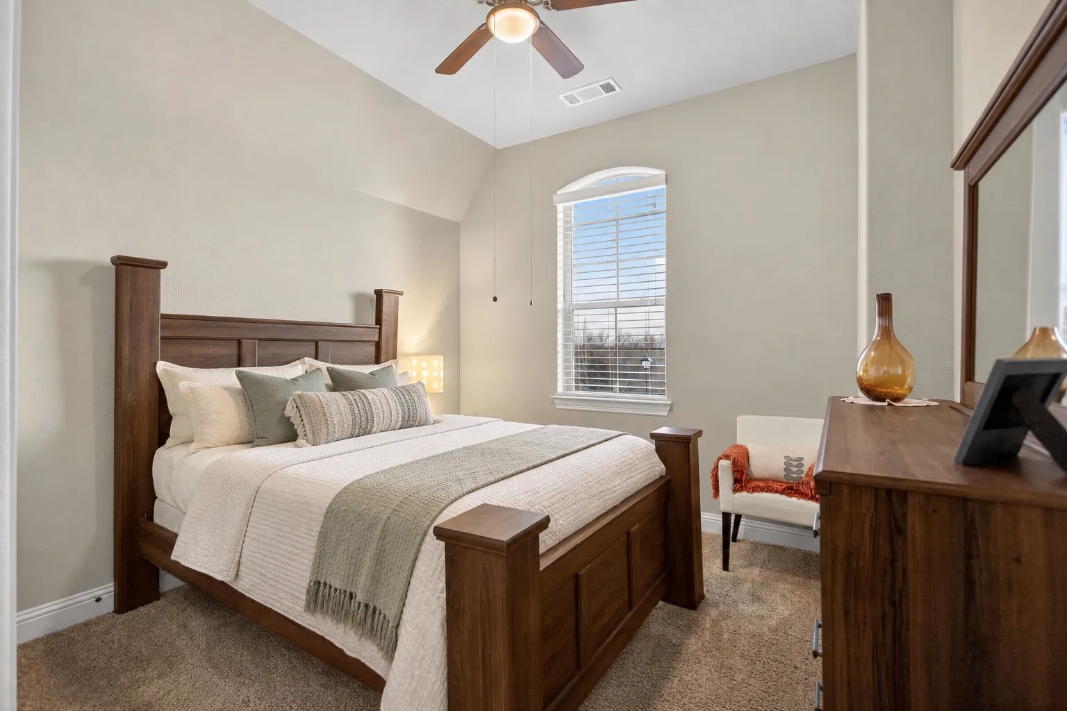 Vaulted ceiling, ceiling fan with integrated lighting, arched window, wood-finish bed frame, and wood-finish dresser with mirror