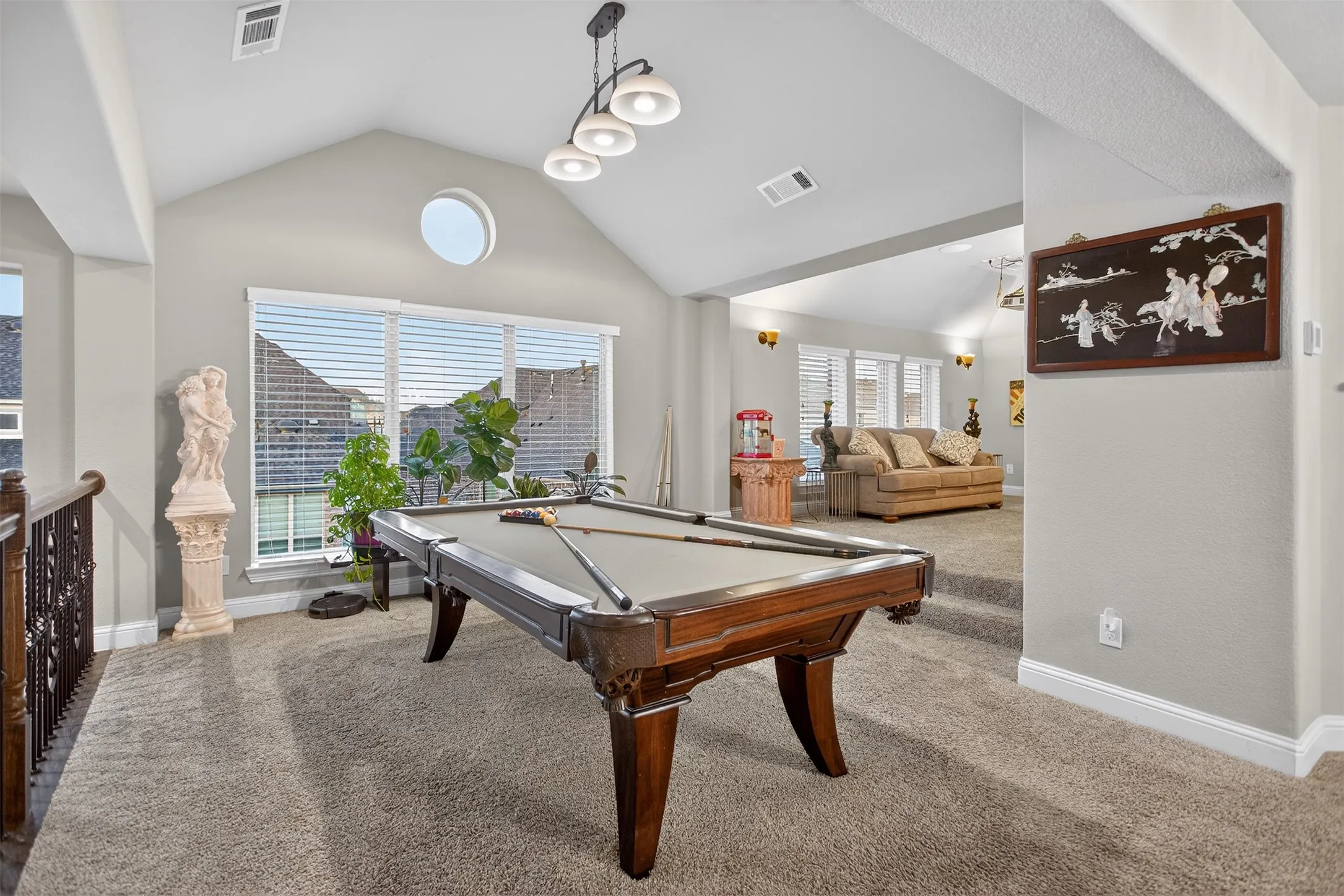 Vaulted ceiling with modern chandelier, round accent window, wall of windows with blinds, and carpeted flooring