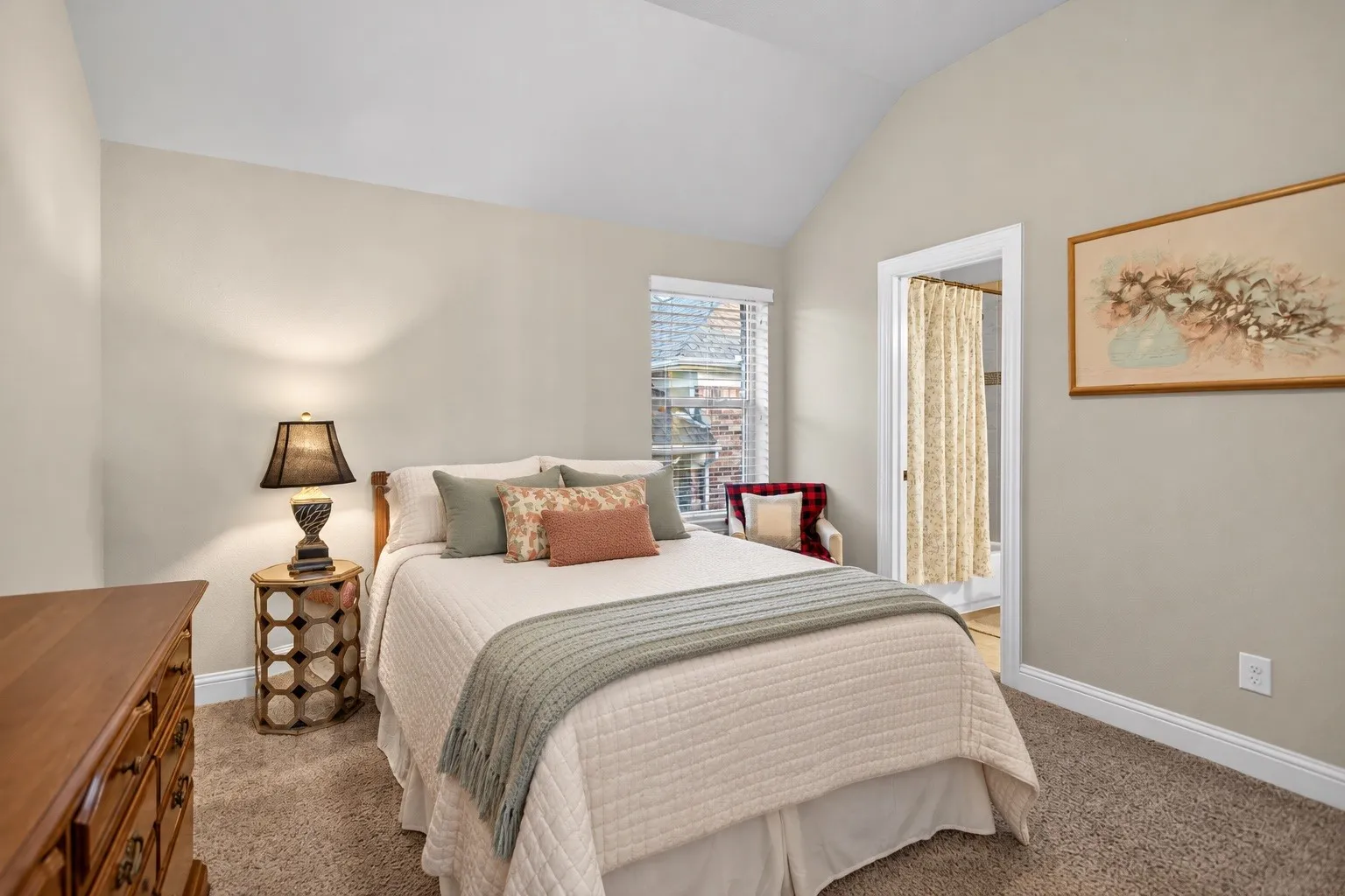 Vaulted ceiling, neutral wall tones, window with horizontal blinds, carpeted flooring, and a doorway leading to an adjoining space