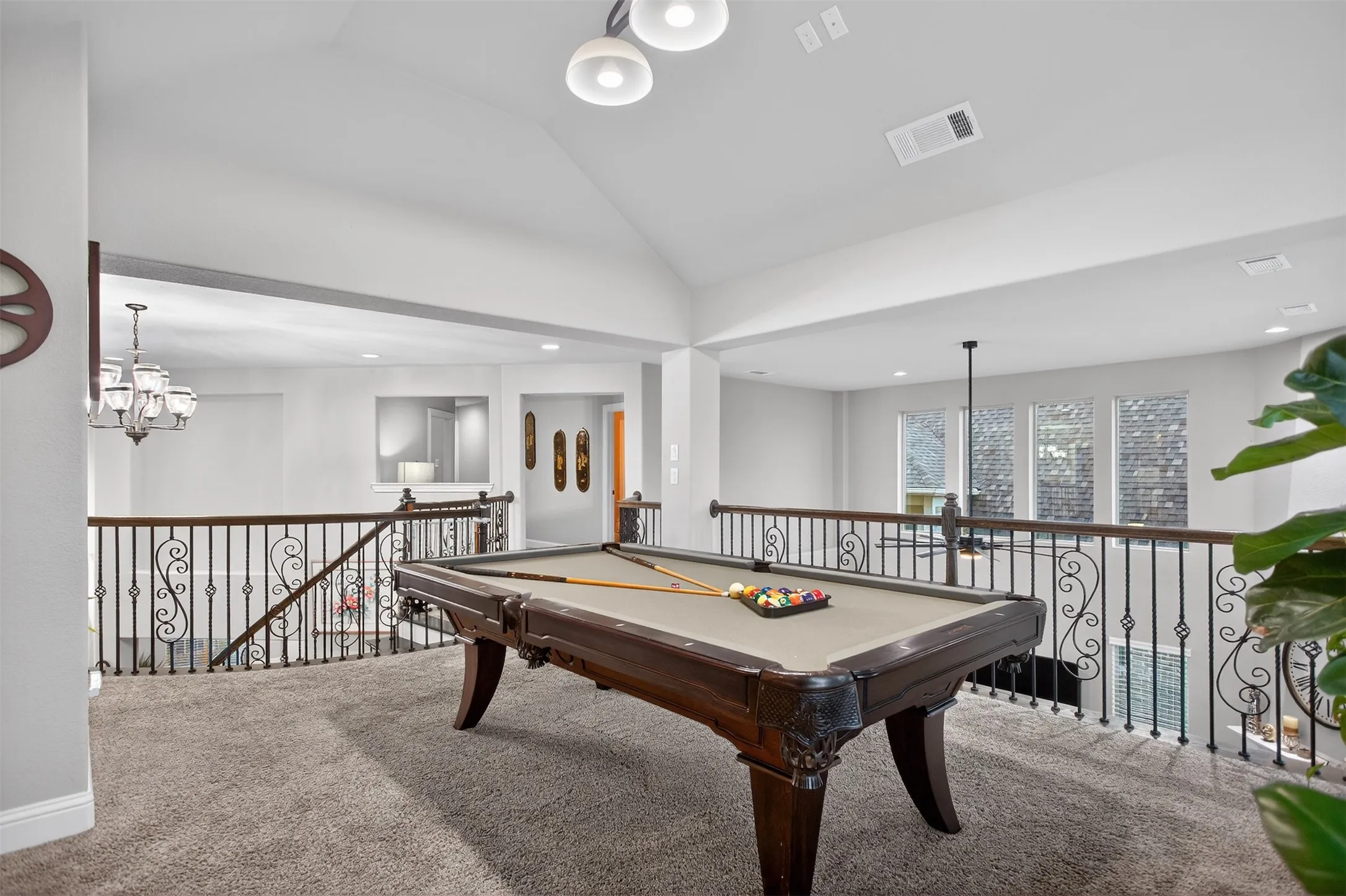 Spacious loft area with vaulted ceilings, recessed lighting, and ornate wrought iron railings