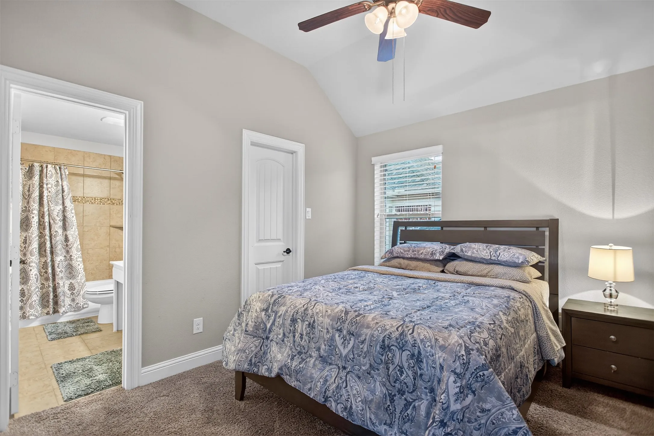 Vaulted ceiling with a ceiling fan, carpeted flooring, and a bedroom door with paneling