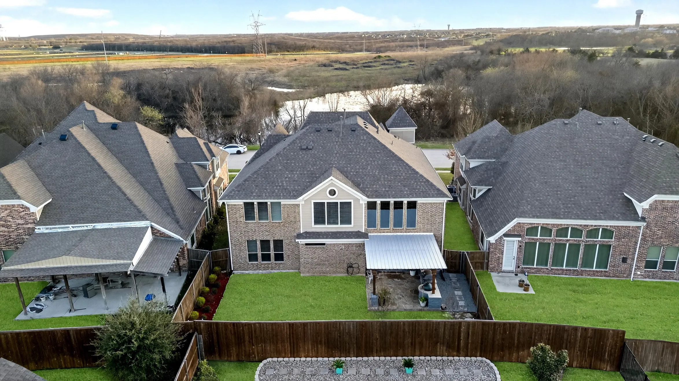 Expansive backyard featuring a manicured lawn, wood fencing, and a covered patio with a metal roof