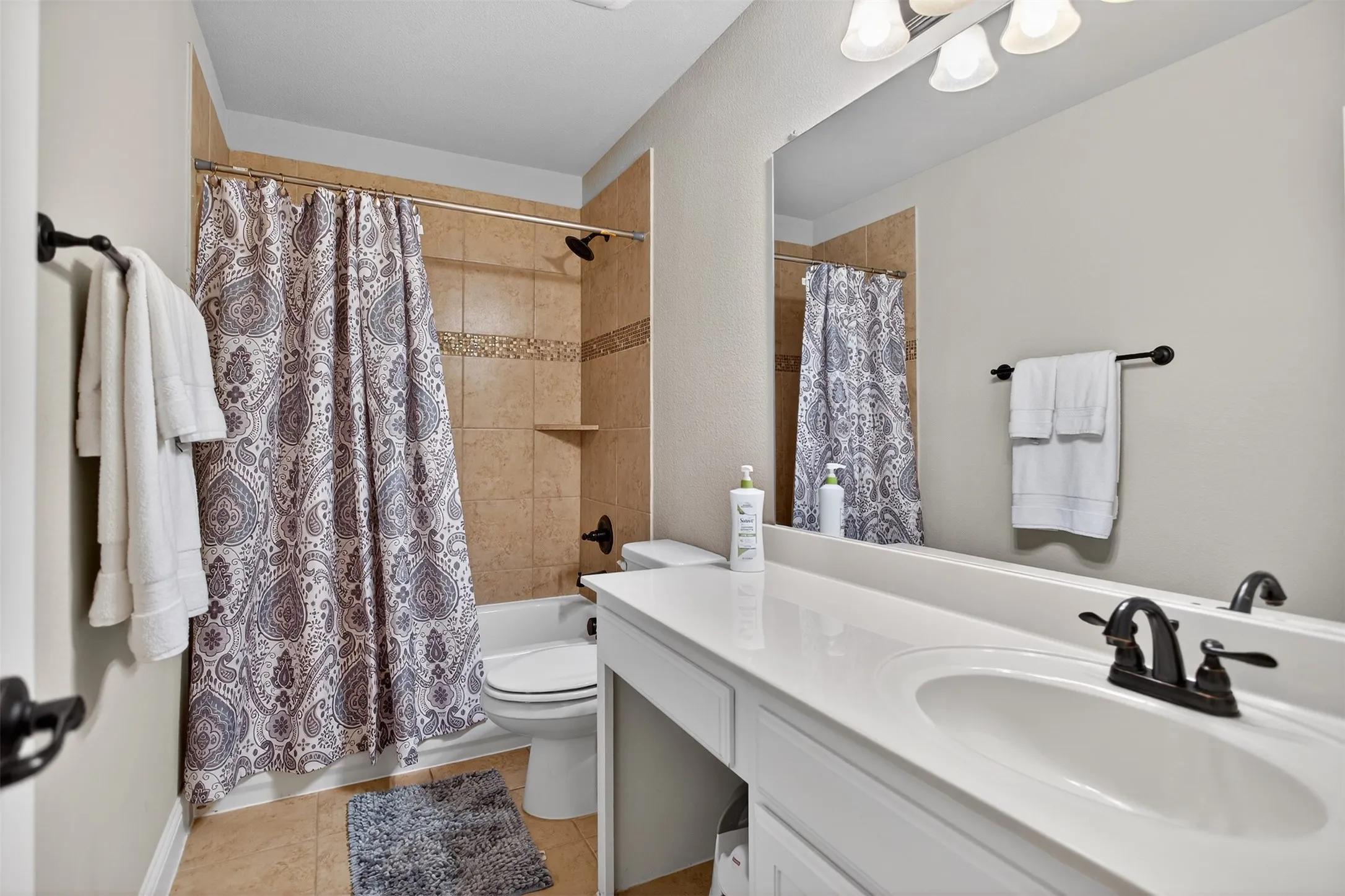 Full-size mirror, integrated vanity lighting, white countertop, dark bronze-finish fixtures, and tile flooring