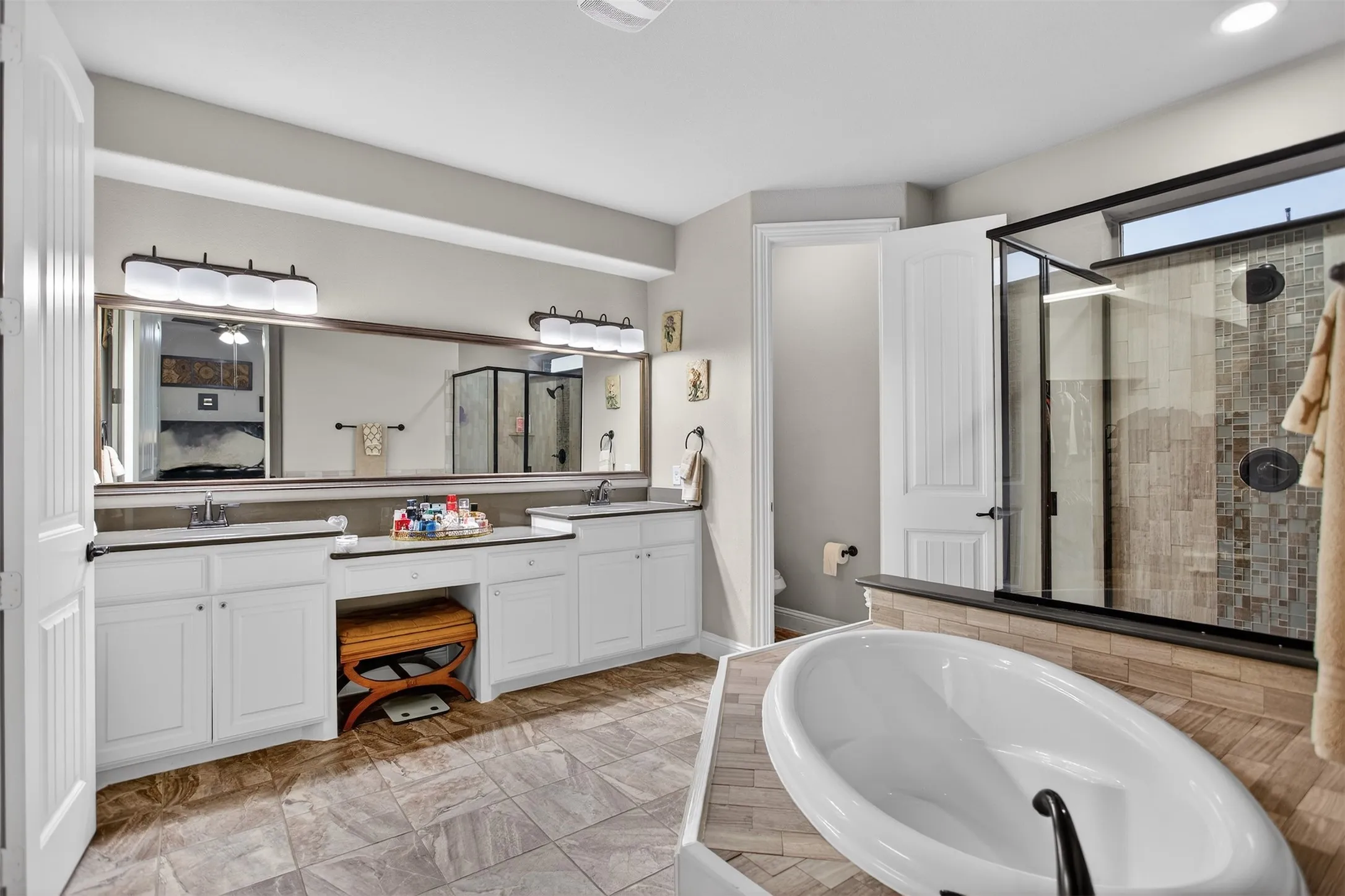 Freestanding soaking tub, walk-in shower with tile surround, double vanity with dual sinks, and large wall-mounted mirror