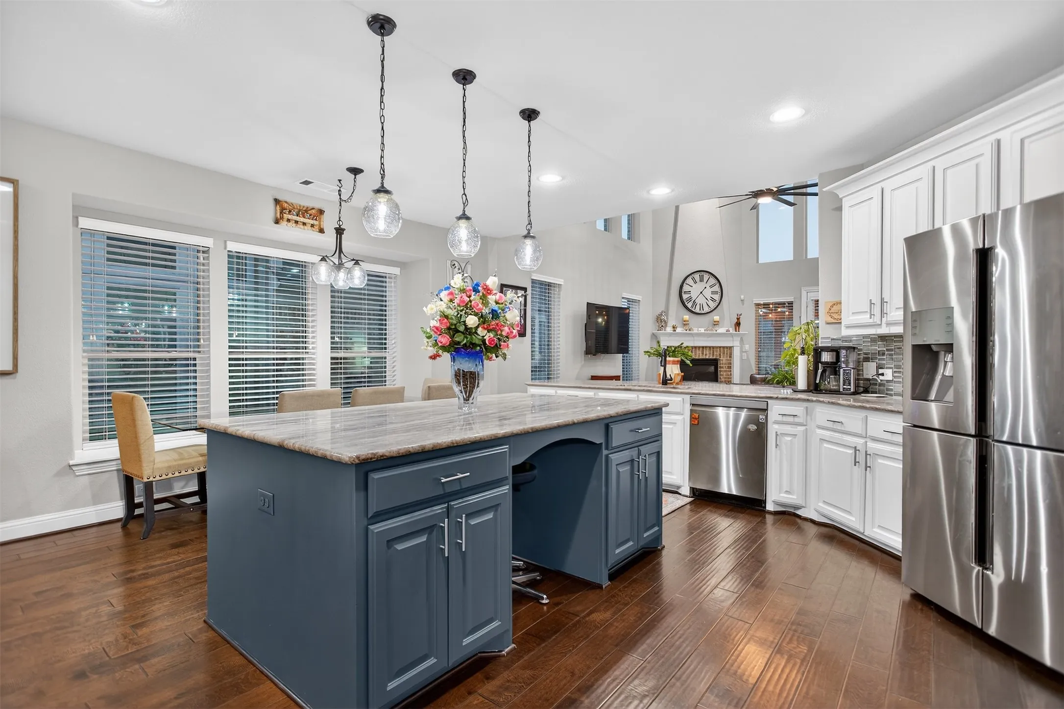 Wood-finish flooring throughout, central island with seating, stainless steel appliances, white cabinetry, and a tile backsplash