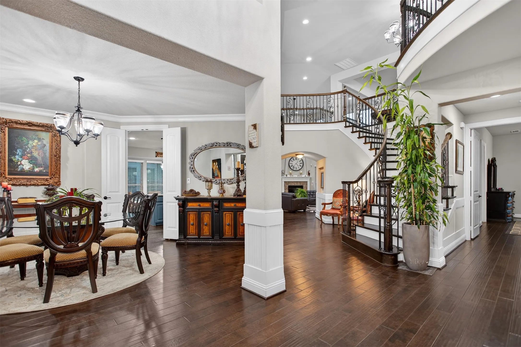 Dark wood-finish flooring, a grand curved staircase with wrought iron balusters, a formal dining area with chandelier, and tall ceilings