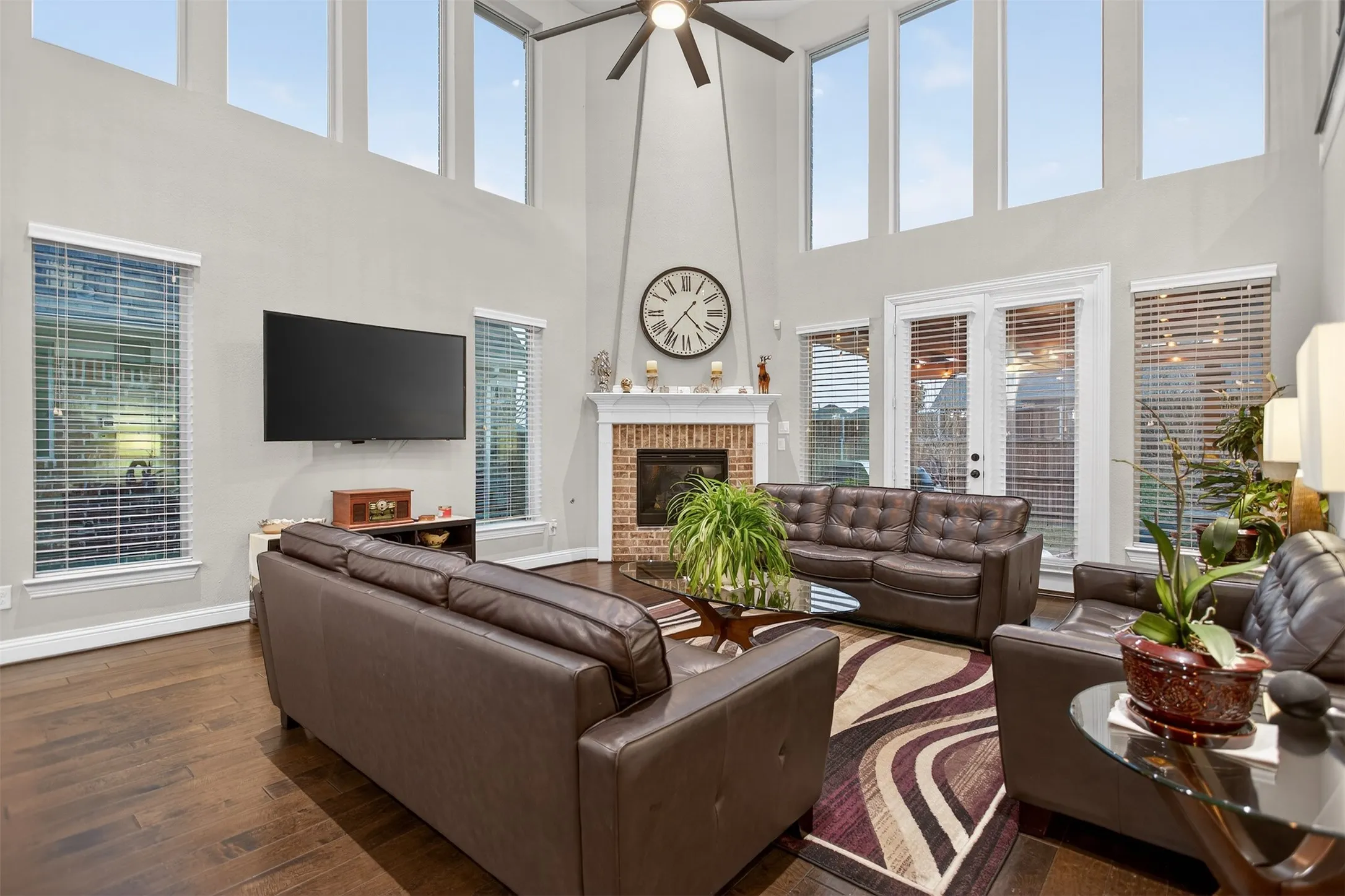 Wood-finish flooring, high ceilings with clerestory windows, ceiling fan, brick fireplace with mantel, and double glass doors