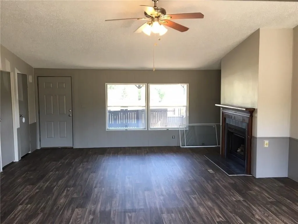 Wood-finish flooring, ceiling fan with light fixture, fireplace with wood mantle, and two windows