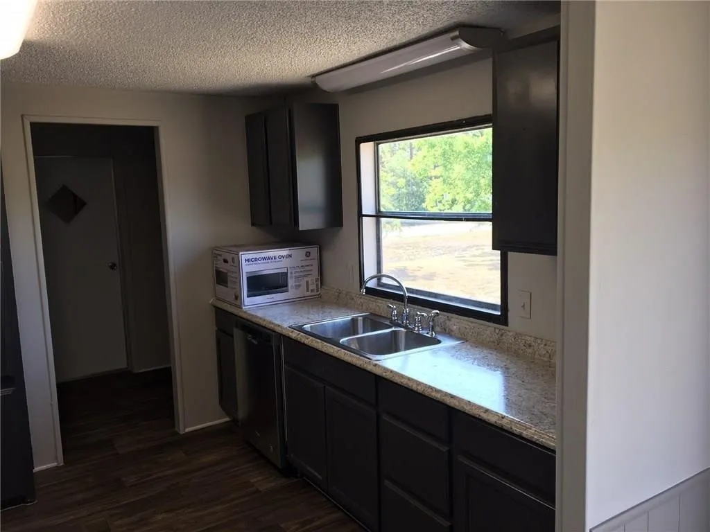 Kitchen featuring dark wood-finish cabinetry, a double basin stainless steel sink, a stainless steel dishwasher, and mottled light-toned countertops
