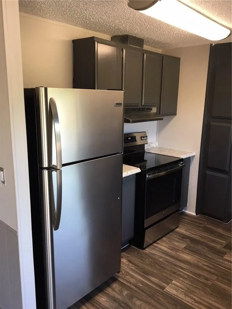 Stainless steel refrigerator, black electric range, black cabinetry, light-toned countertops, and wood-finish flooring