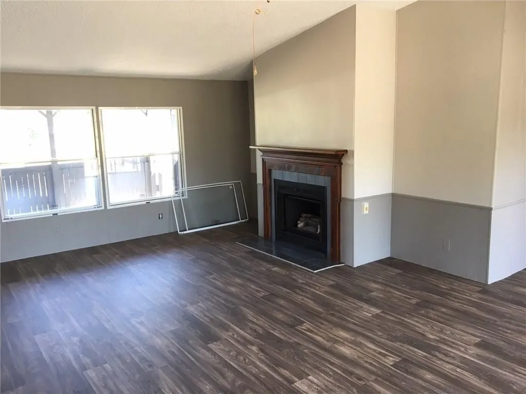 Wood-finish flooring, fireplace with a wood surround, dual windows, and vaulted ceiling