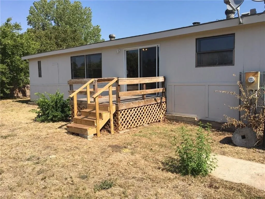 Rear exterior featuring a wooden deck with railing, sliding glass door, and a concrete pathway