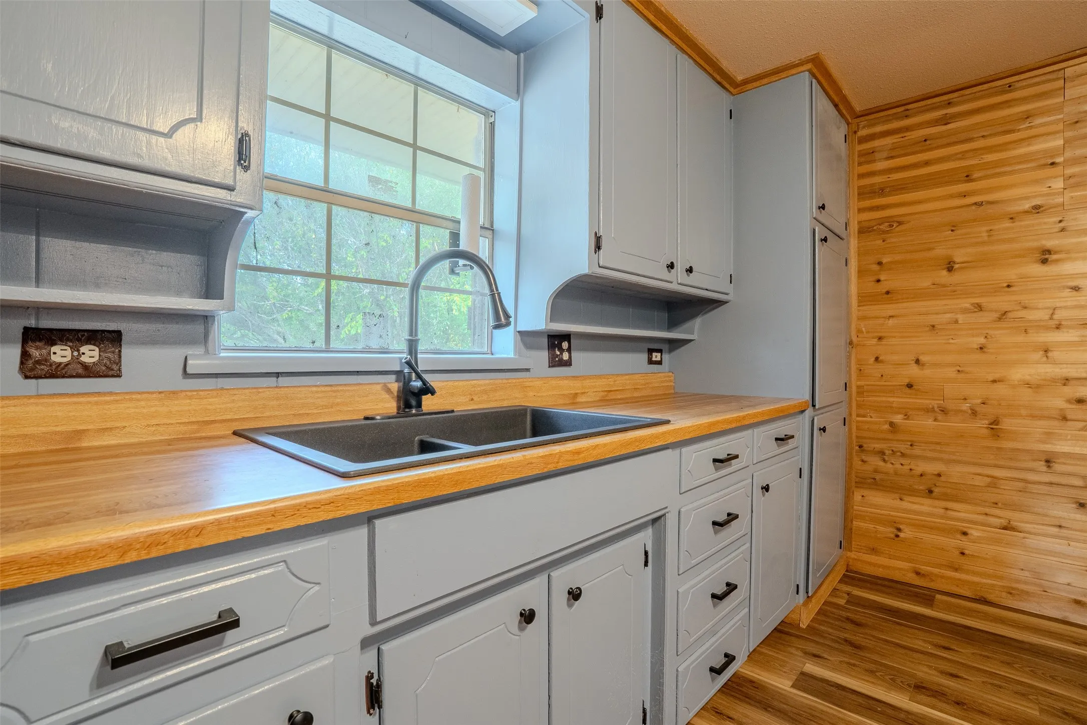 Light gray cabinetry with black hardware, wood-finish countertops, and a double basin sink with a gooseneck faucet