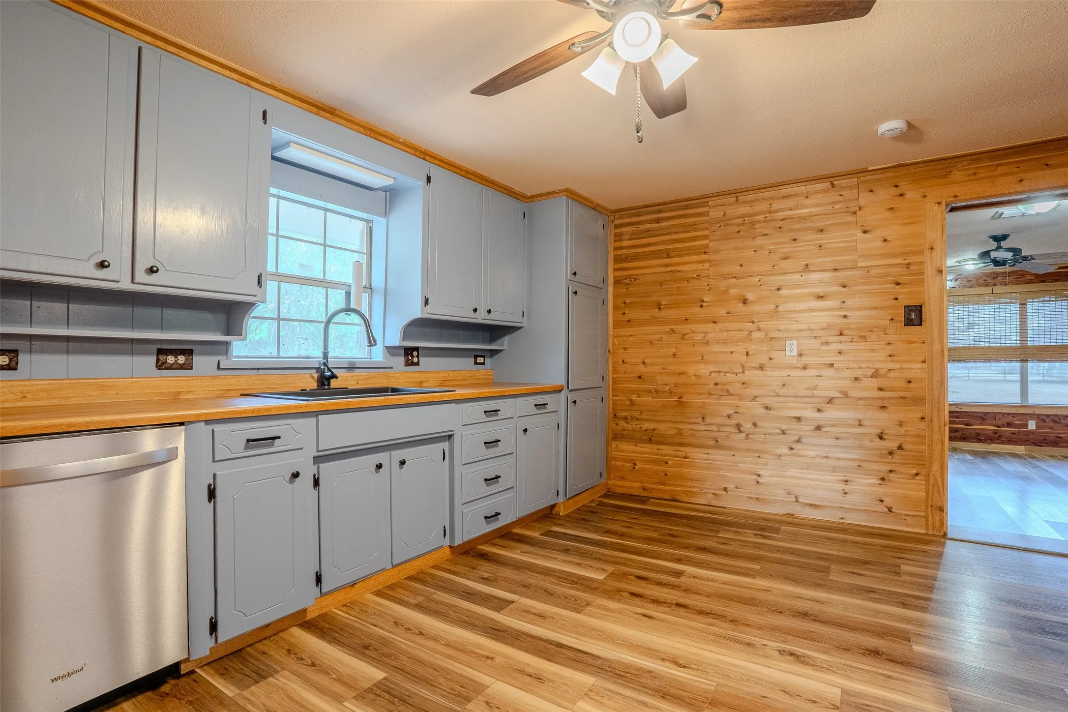 Wood-finish flooring, light blue cabinetry with dark hardware, wood countertops, stainless steel dishwasher, and wood-paneled accent wall
