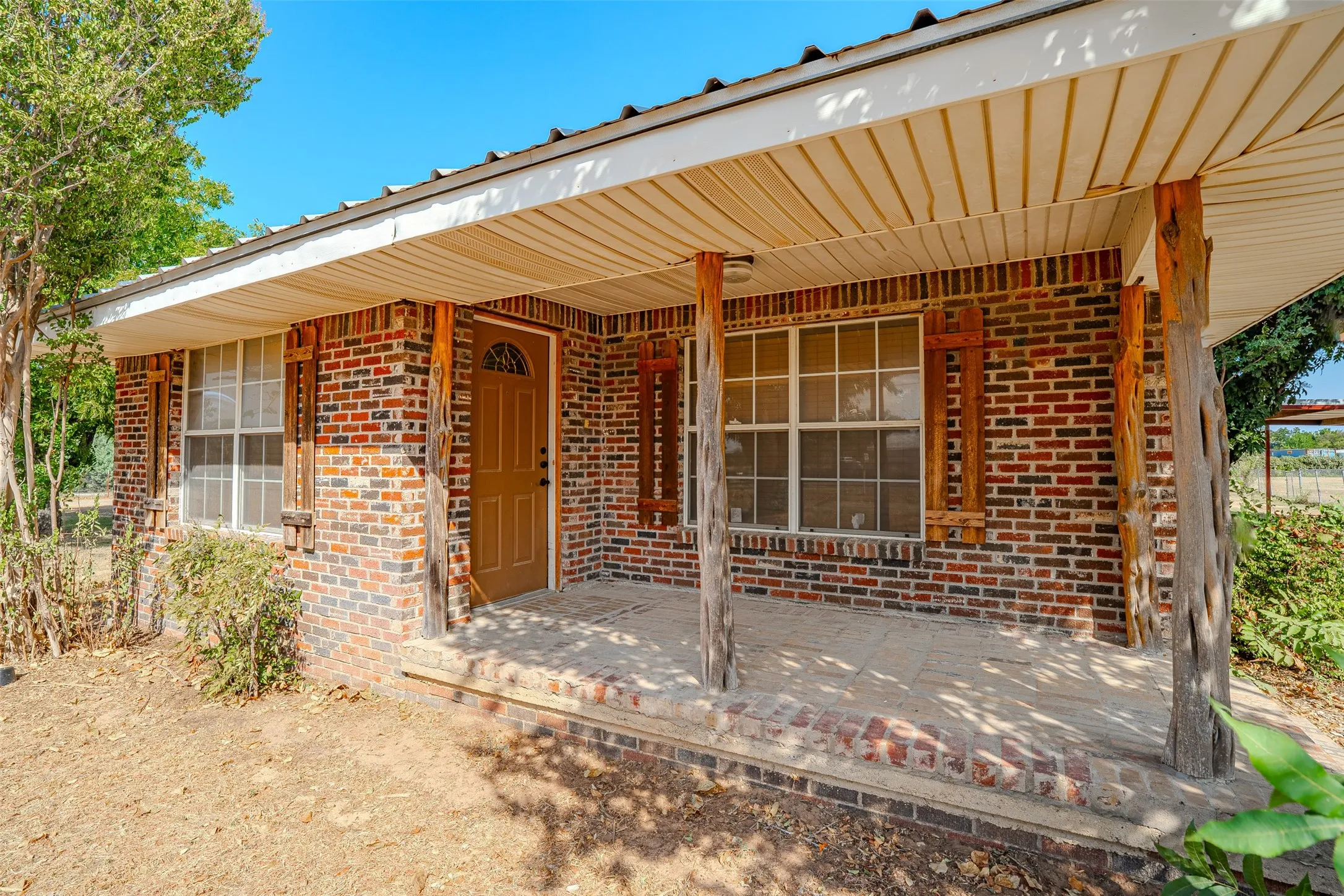 Brick exterior with covered front porch, wood-finish columns, and a wood-finish entry door with decorative glass inserts