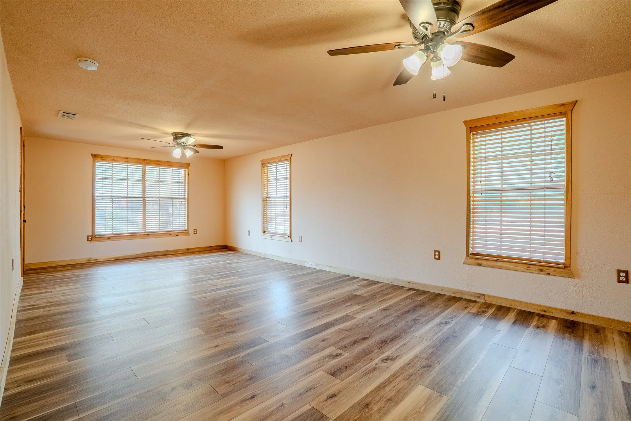 Spacious room featuring wood-finish flooring, multiple windows with blinds, and two ceiling fans with light fixtures