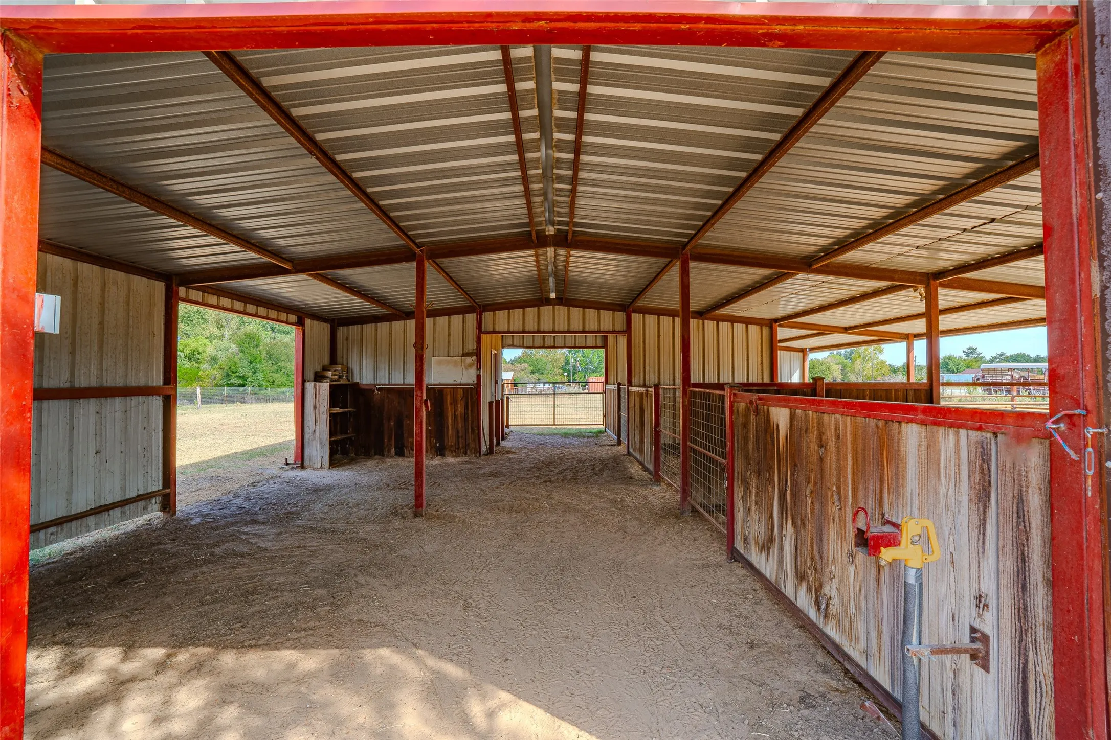 Metal barn structure featuring a corrugated roof, red-painted metal framing, and partial wood-paneled stalls