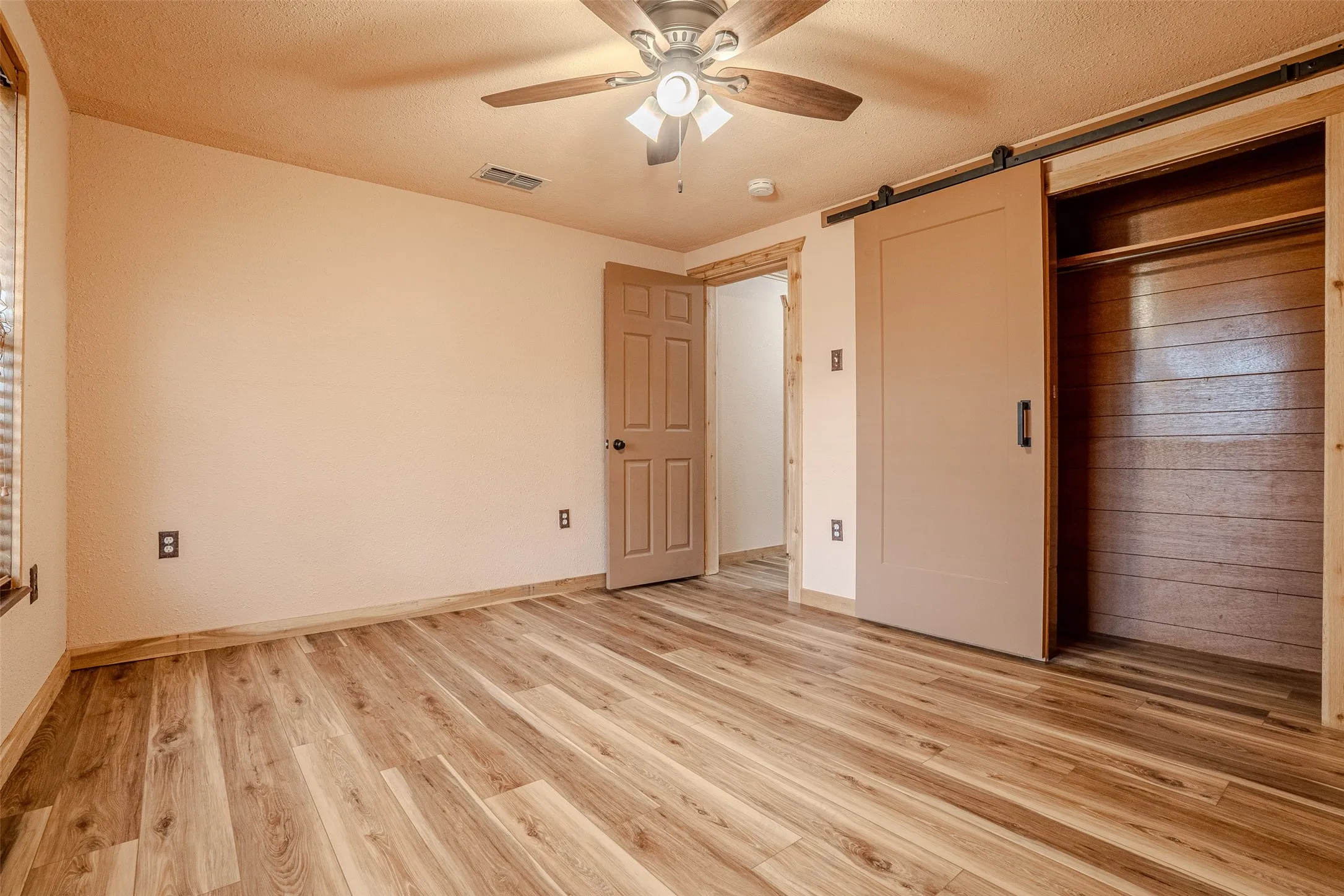 Wood-finish flooring, ceiling fan with integrated lighting, wood trim accents, and a barn door closet with shiplap-style interior