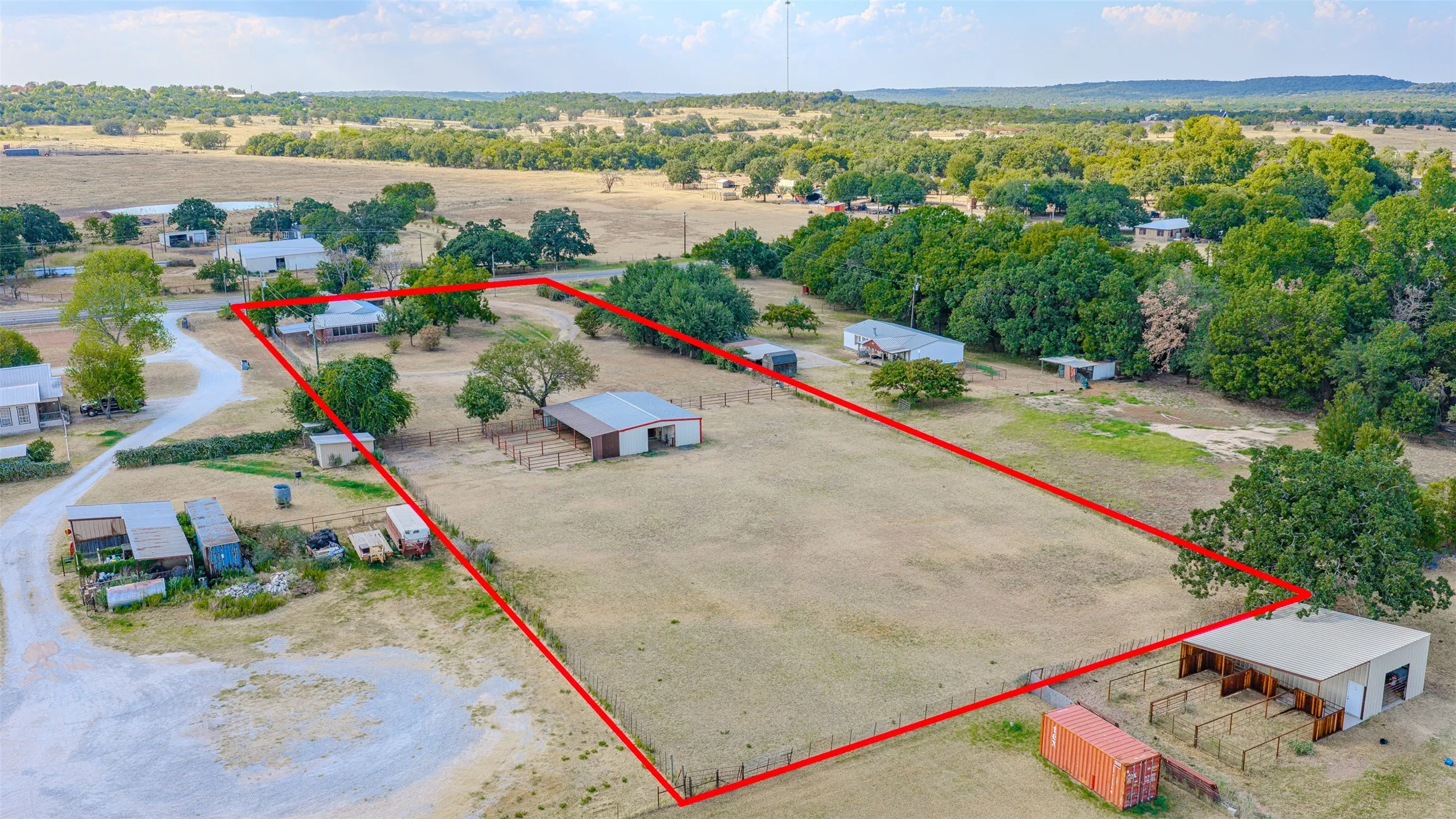 Expansive property featuring a single-story residence, multiple outbuildings, mature trees, and a large open field