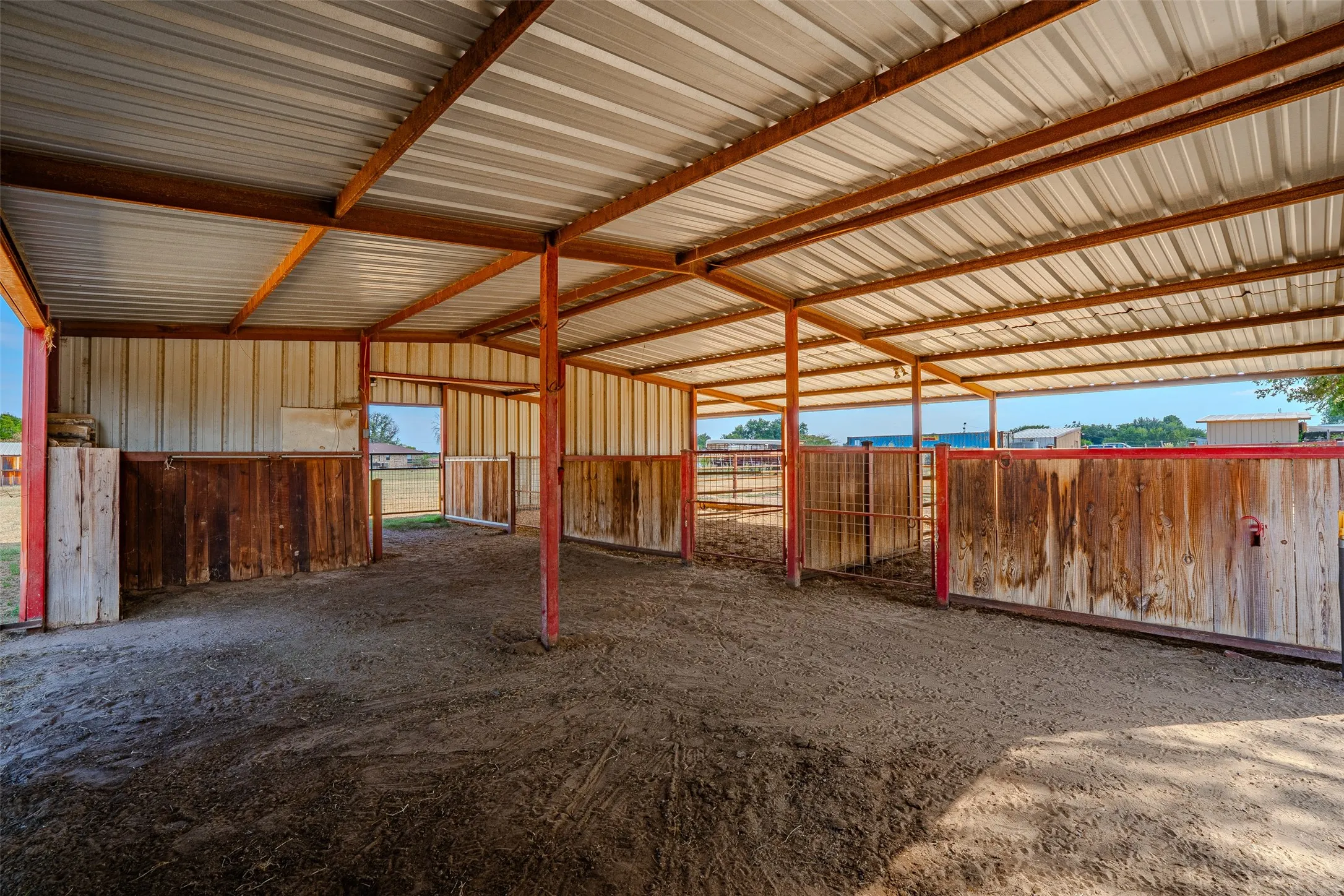 Sheltered outdoor structure with a corrugated metal roof, wood-paneled partitions, and metal support beams