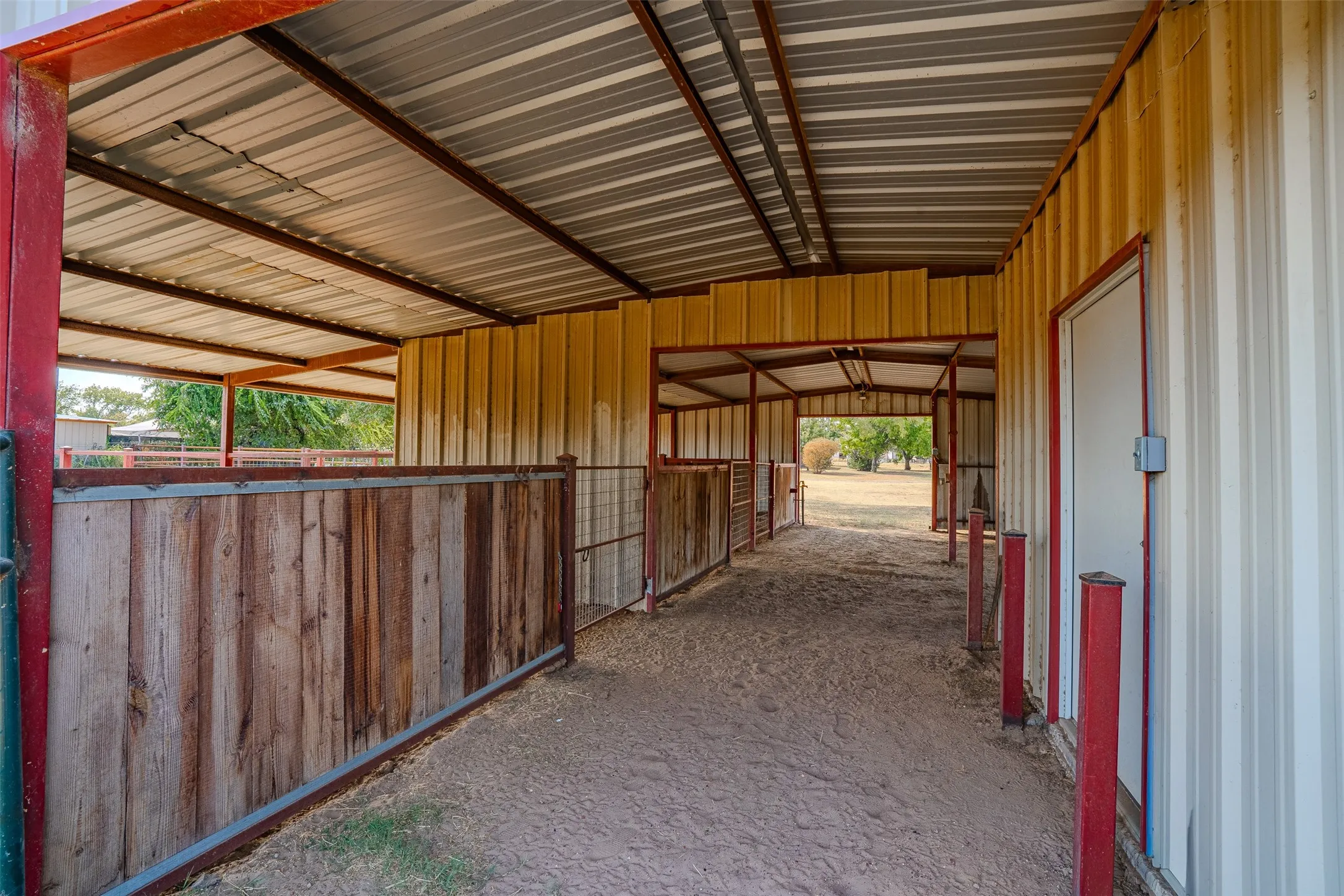 Covered outdoor structure with a metal roof, corrugated metal siding, and wood fencing