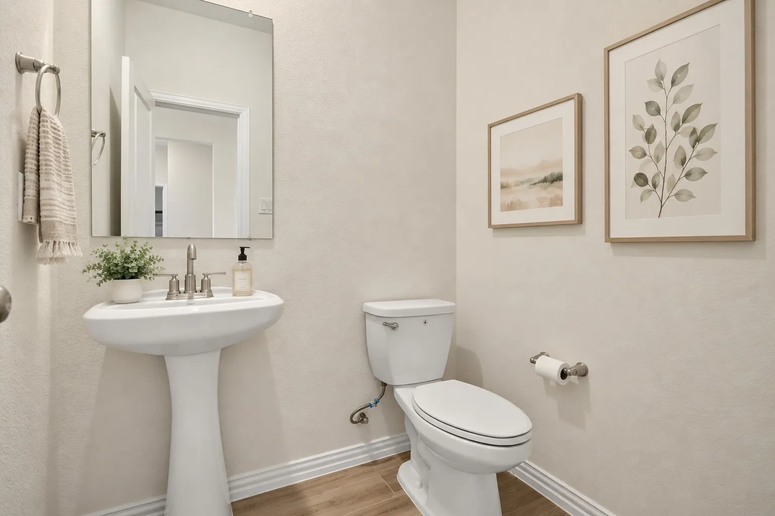 Pedestal sink with a polished chrome faucet, rectangular mirror, and wood-finish flooring