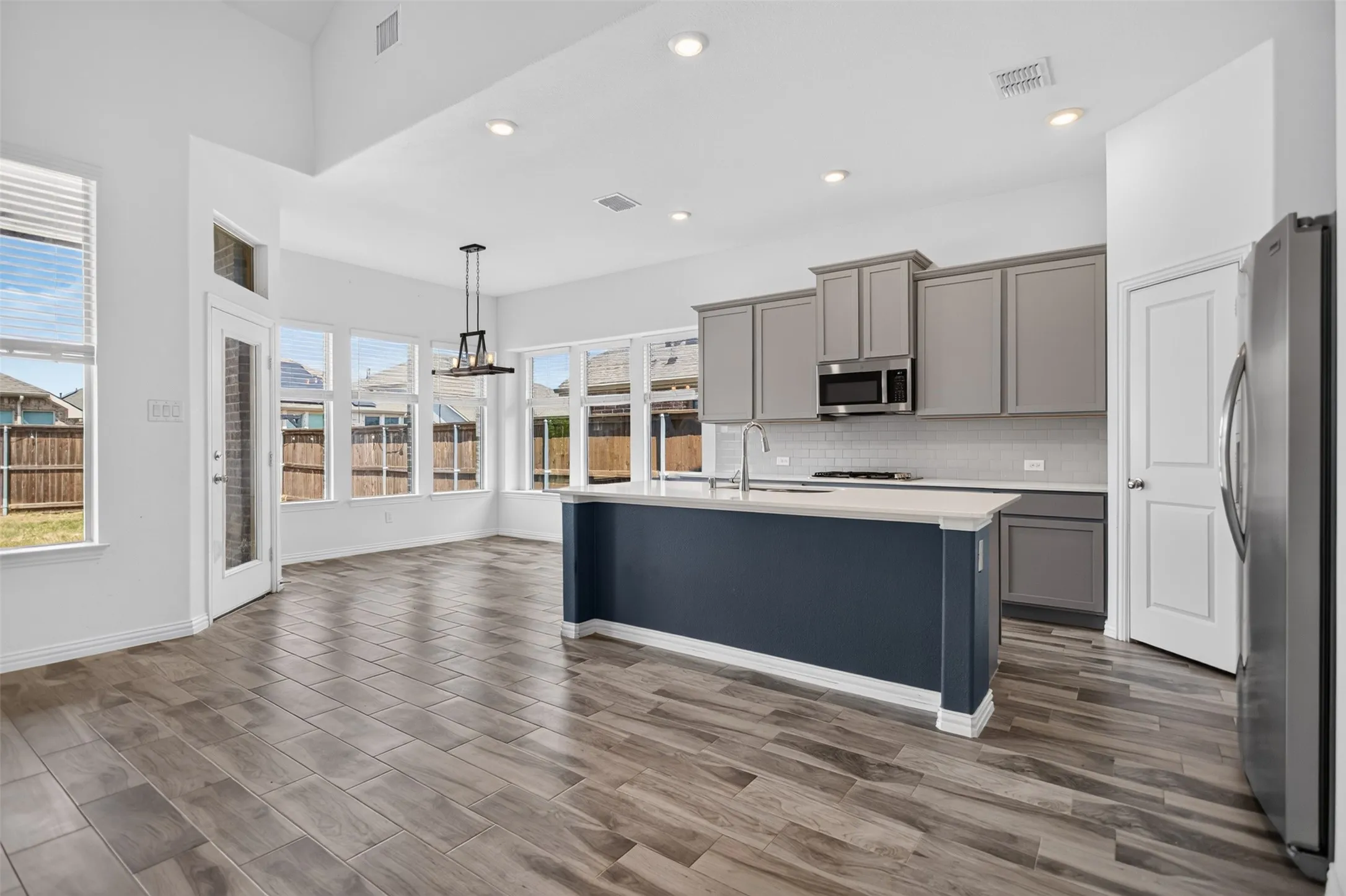 Open-concept kitchen and dining area featuring wood-finish flooring, a two-tone kitchen island with a white countertop, gray cabinetry, and recessed lighting