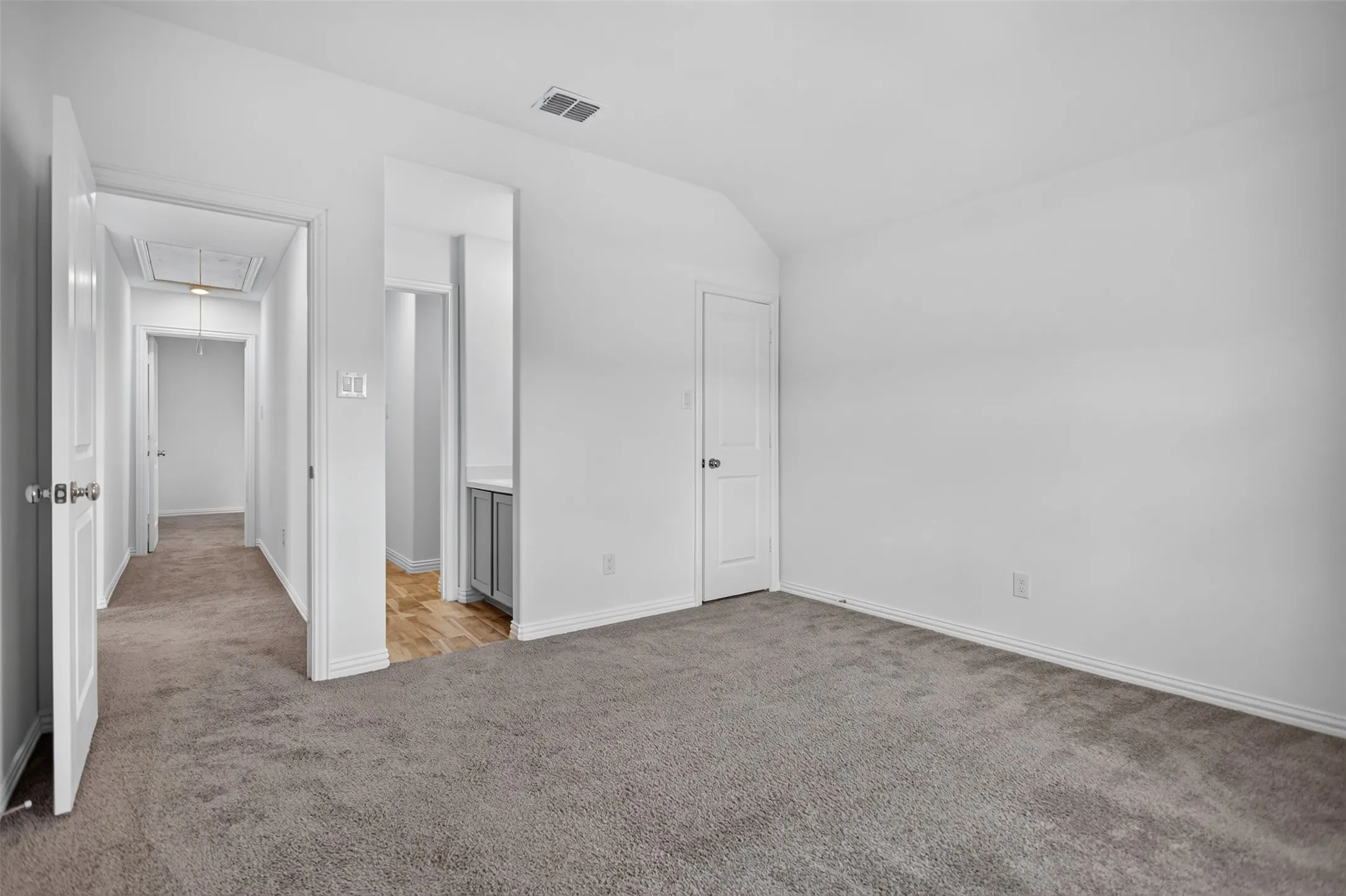 Spacious room featuring neutral carpeting, white interior doors, and a vaulted ceiling
